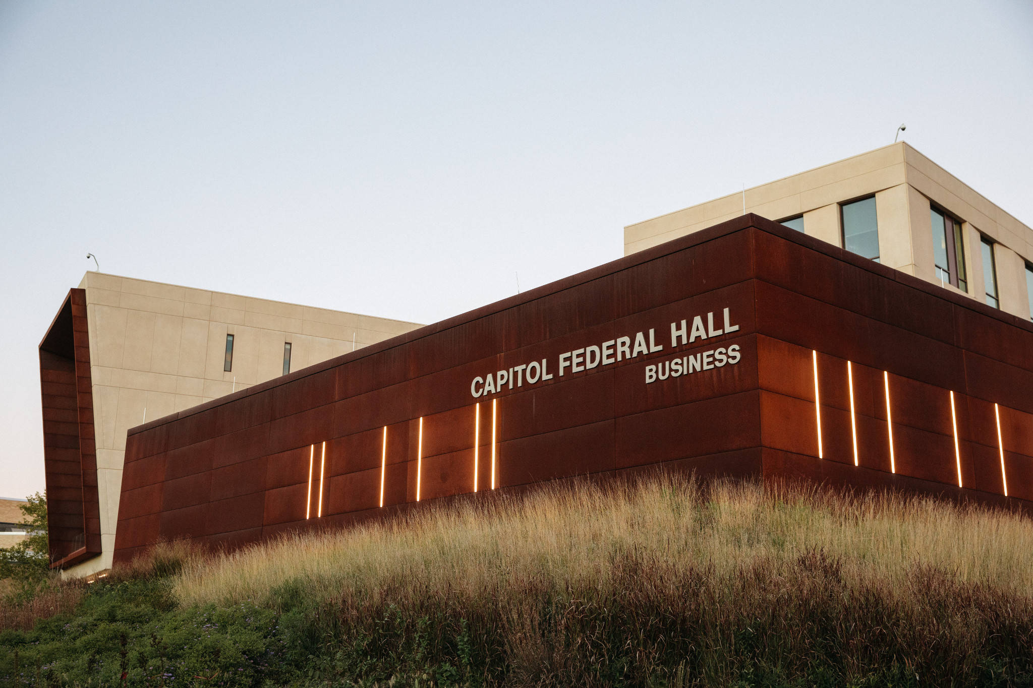 學校 桌布 壁紙 — 現代Capitol Federal Hall建築，帶有鏽色金屬外牆和發光的垂直燈光，映襯著黃昏時的乾草。