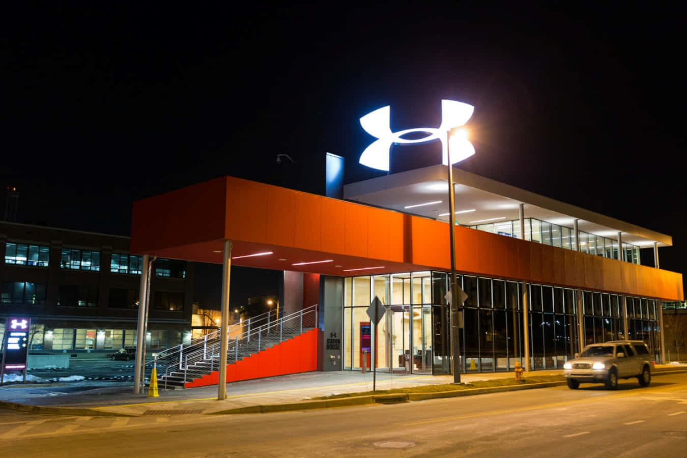 Under Armour 桌布 壁紙 — 現代Under Armour商店在夜間亮起，以鮮明的橙色點綴和發光標誌映襯著黑暗的天空。