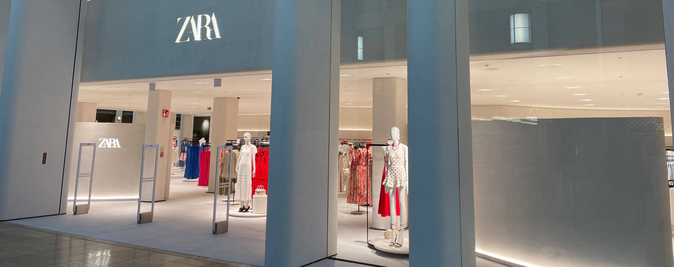 Zara 桌布 壁紙 — 現代Zara商店入口，人體模型在明亮室內燈光下展示色彩繽紛的服裝。