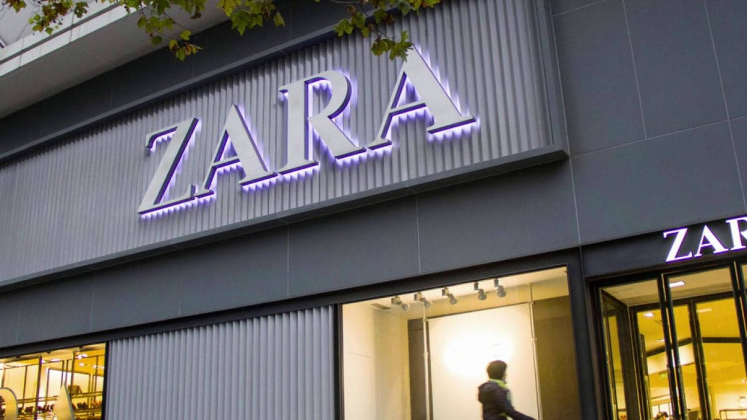 Zara 桌布 壁紙 — 現代Zara商店外牆，灰色波紋板及玻璃窗上帶有發光的紫色霓虹燈標誌。