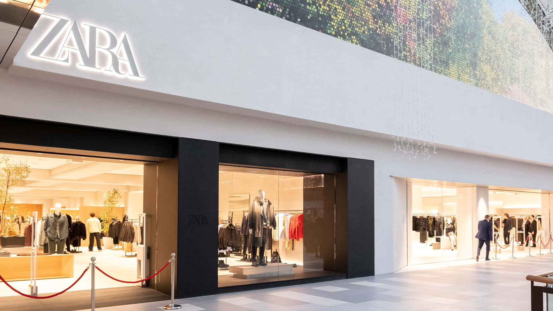 Zara 桌布 壁紙 — 現代Zara店鋪外牆，透過大型玻璃窗展示明亮室內燈光下的模特兒公仔和衣物架。