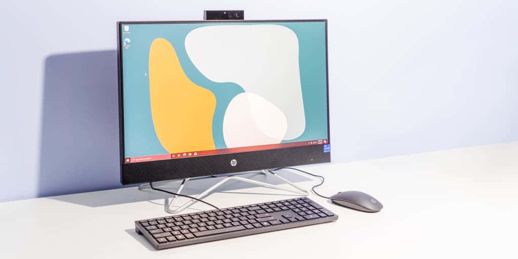 HP 桌布 壁紙 — 現代一體式桌面電腦，螢幕上顯示抽象桌布，旁邊有鍵盤和滑鼠，放在潔白的桌子上。