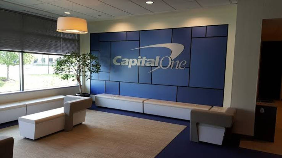 桌布 壁紙 — 現代企業大廳，設有白色模塊化座椅、帶有 Capital One 標誌的藍色特色牆，以及可俯瞰綠化景觀的大型窗戶。