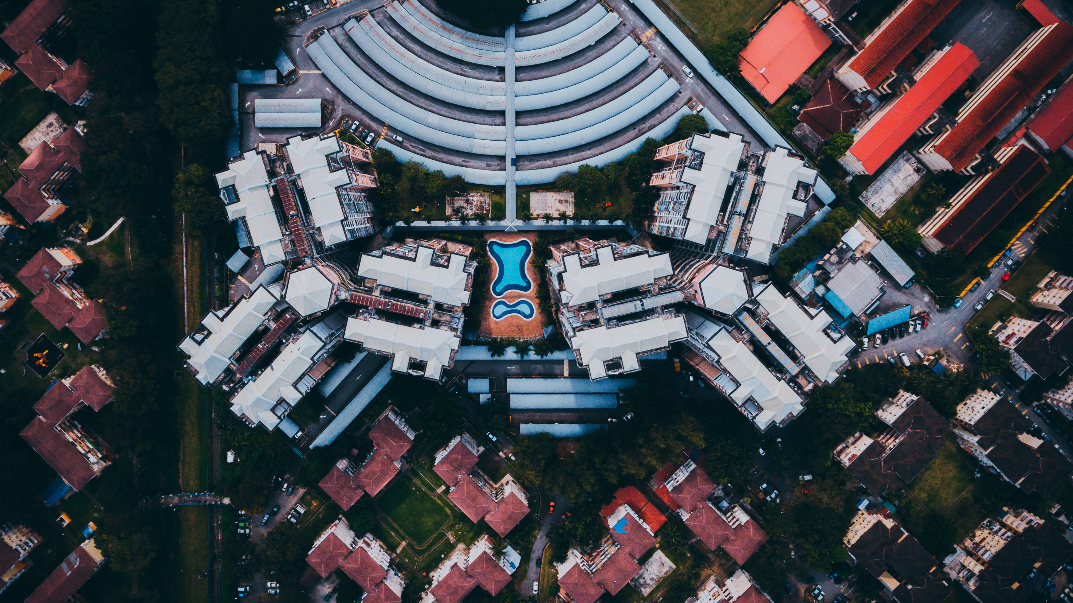 Unique 桌布 壁紙 — 現代住宅區的鳥瞰圖，擁有曲線建築和中央游泳池，周圍環繞著樹木和紅頂房屋。