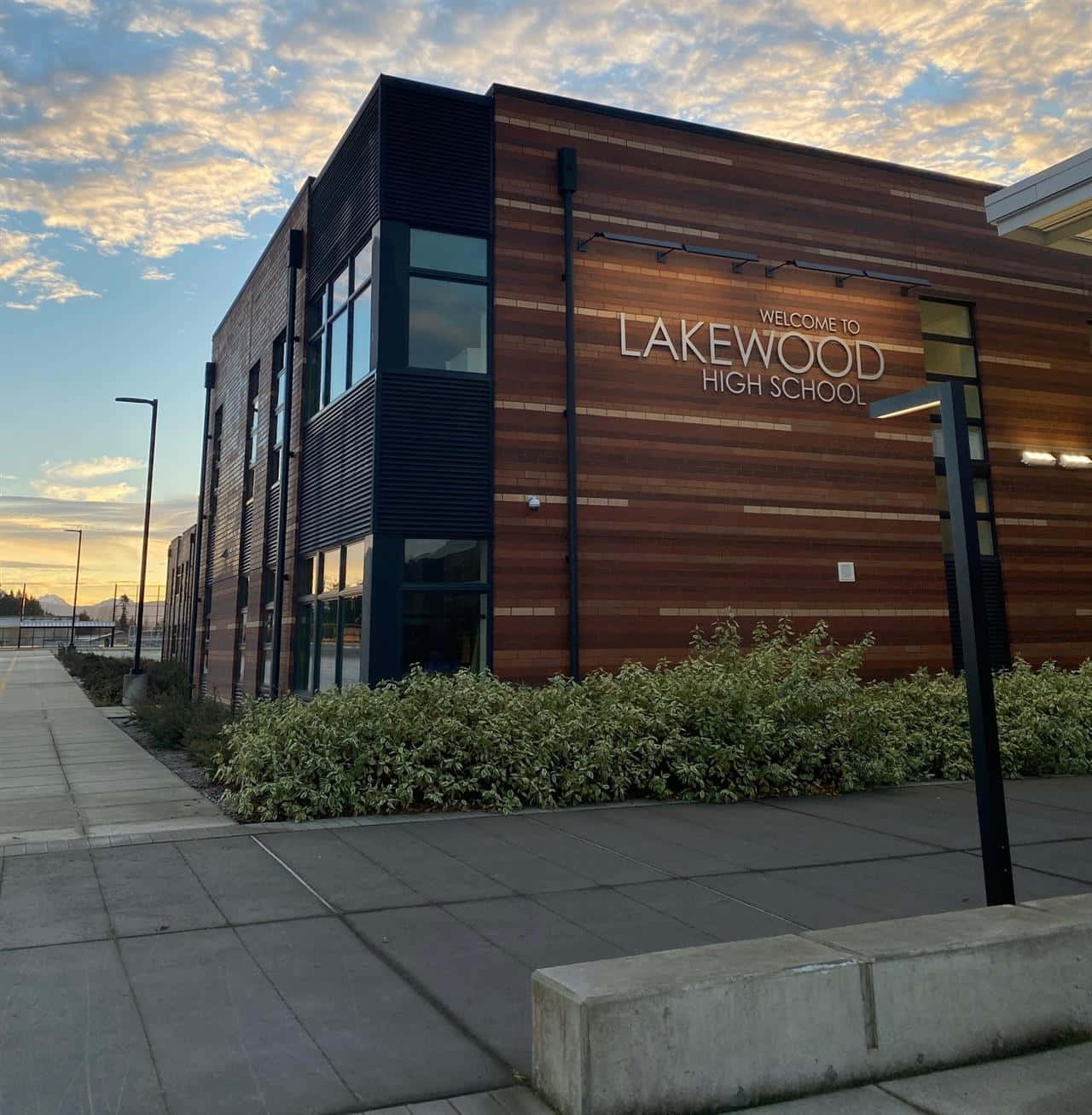 High School 桌布 壁紙 — 現代化的 Lakewood 高中建築，採用木材和黑色鑲板，在金色夕陽天空下。