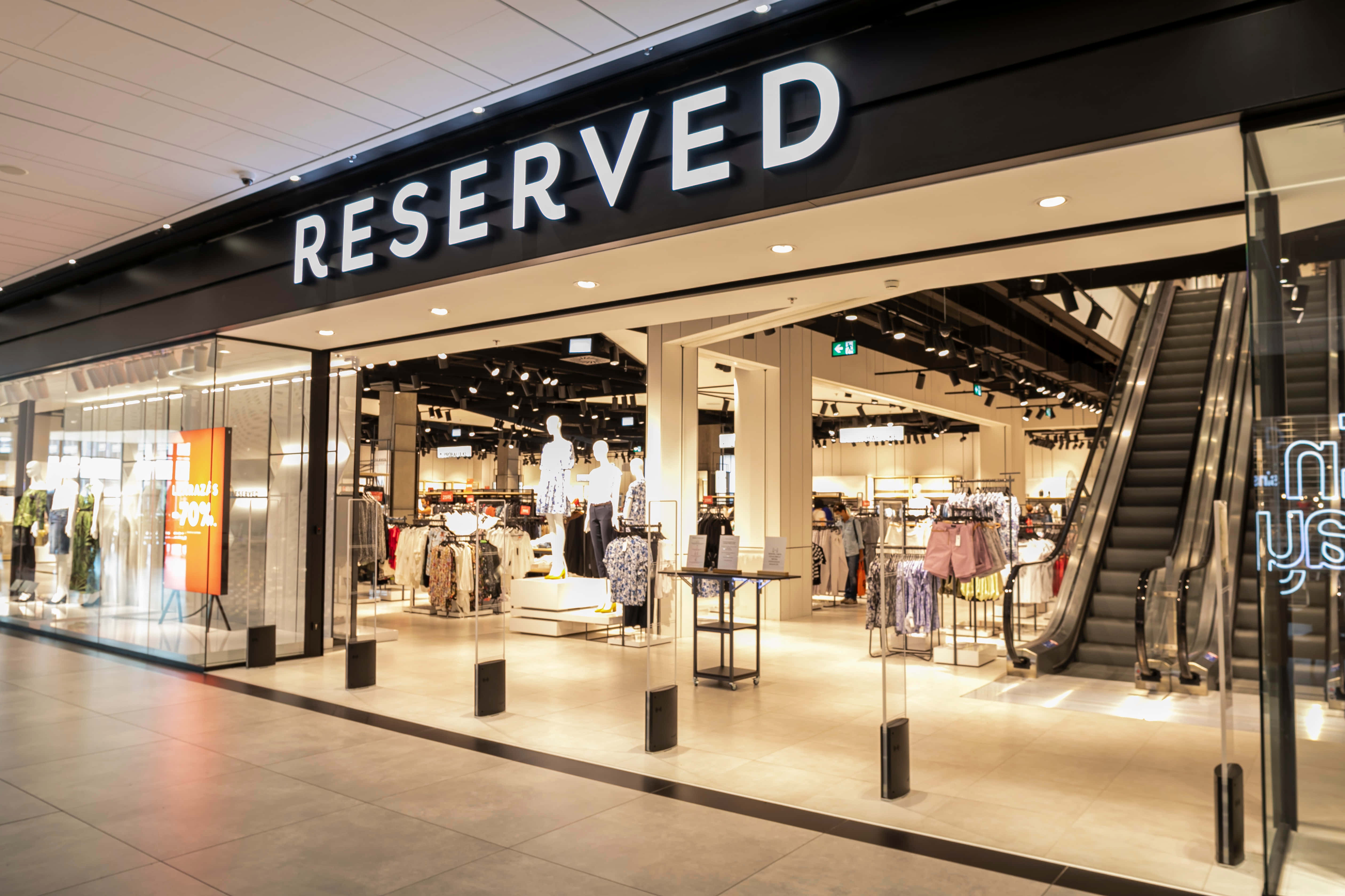 Reserved 桌布 壁紙 — 現代化的Reserved服裝店，設有玻璃牆、人體模型、貨架和自動扶梯，室內光線明亮。