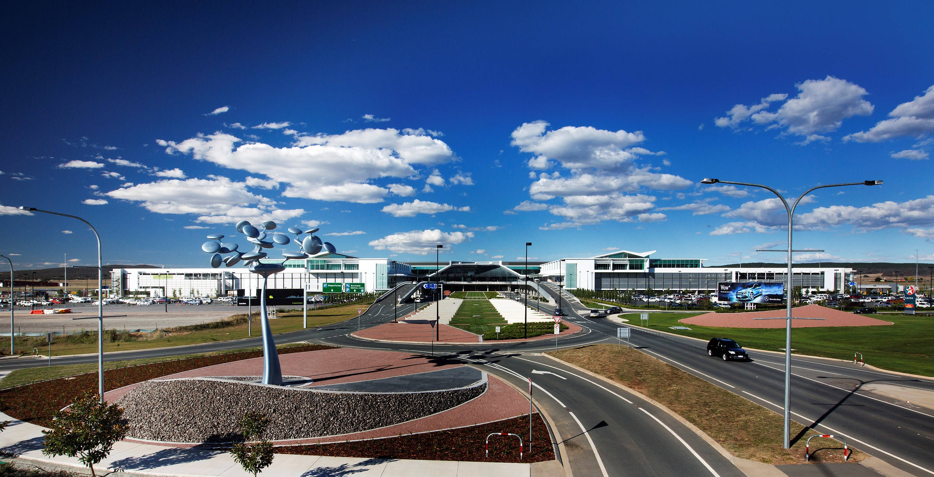 Airport 桌布 壁紙 — 現代化的機場航廈，在明亮的藍天下有蓬鬆的白雲，一條彎曲的道路通往入口。