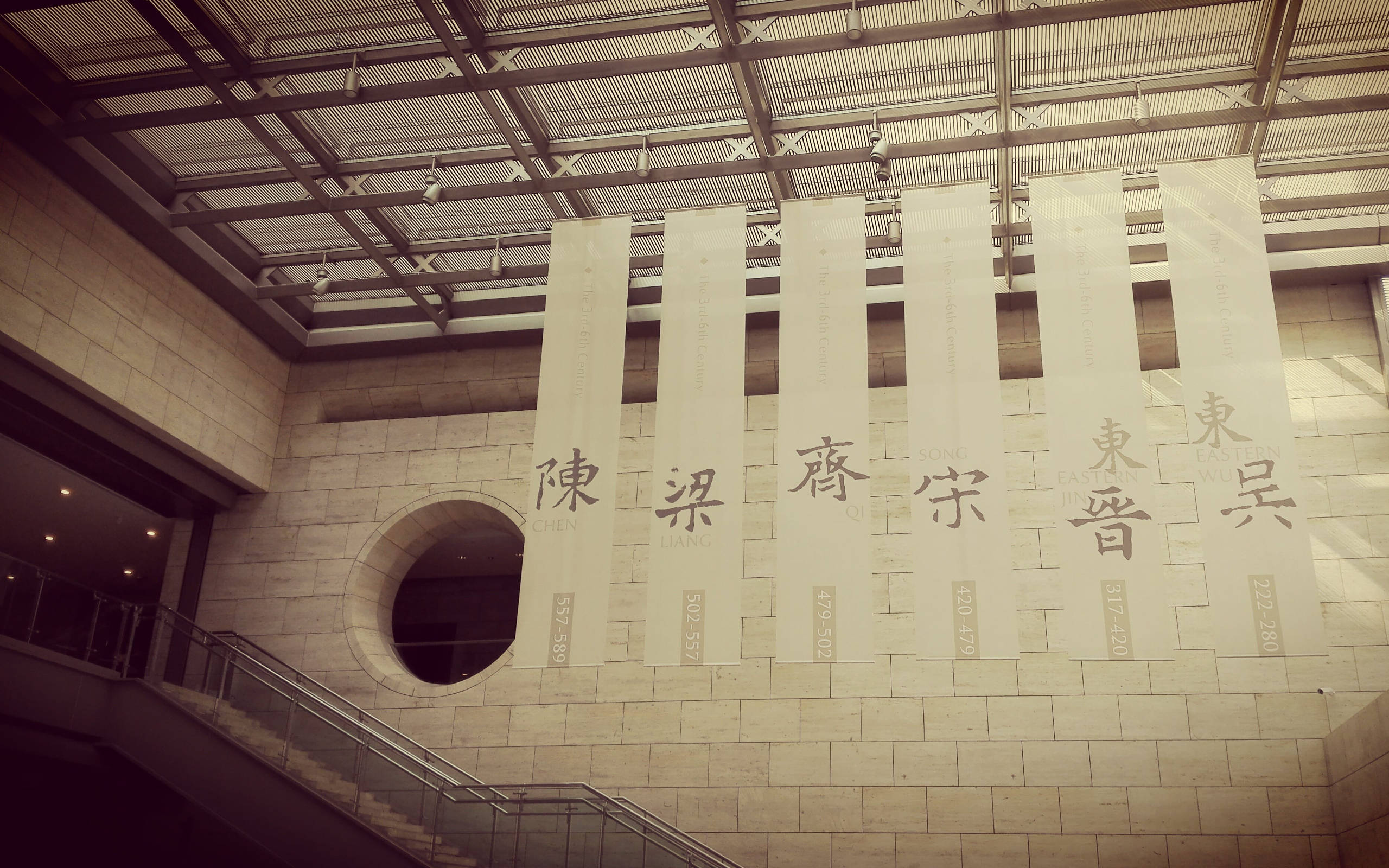 Nanjing 桌布 壁紙 — 現代博物館的棕褐色調室內景觀，掛有展示中文字元和日期的橫幅，背景為石牆和樓梯。