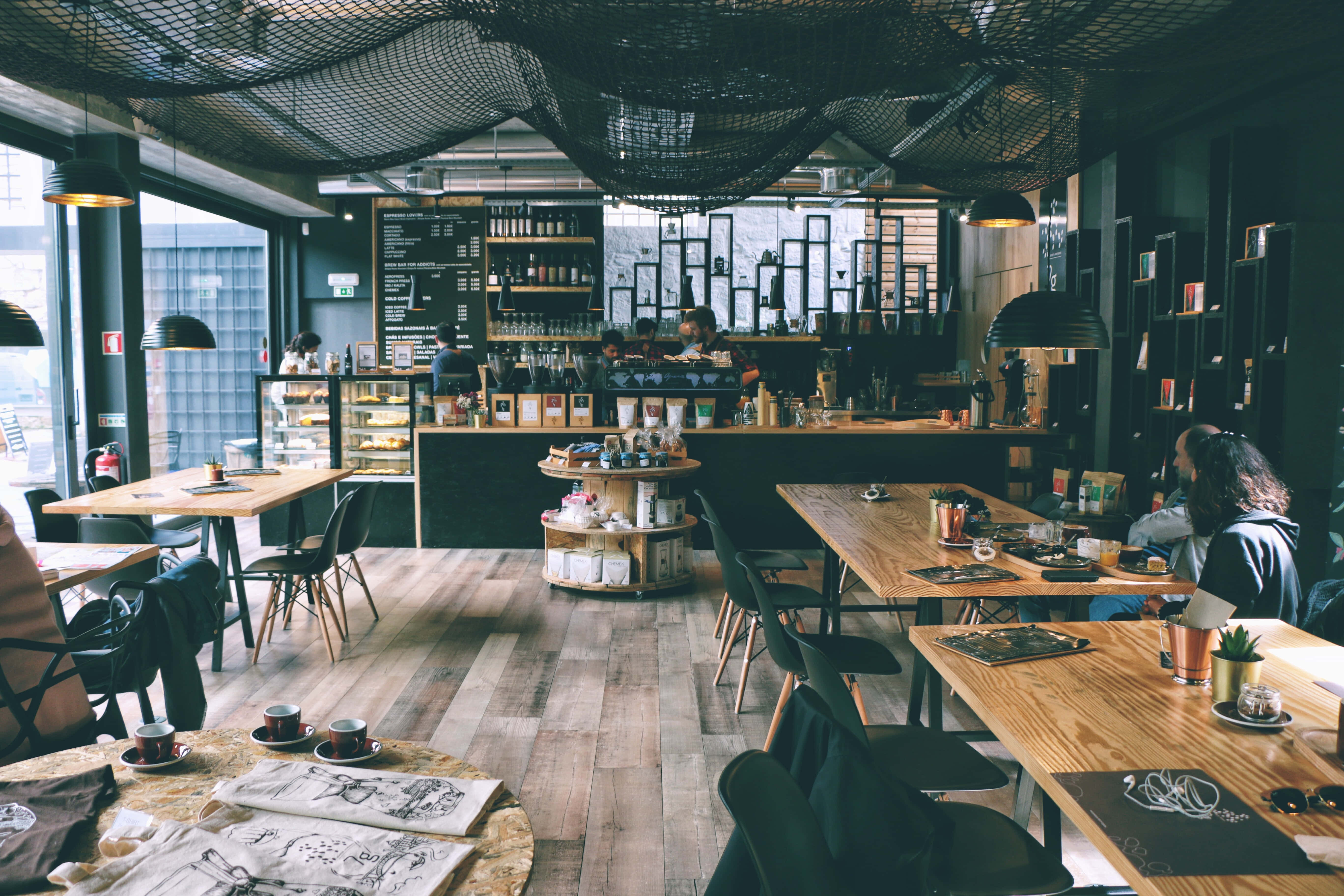 Coffee Aesthetic 桌布 壁紙 — 現代咖啡店，配有木桌、黑色椅子和網狀天花板燈，為顧客投射溫暖的光芒。