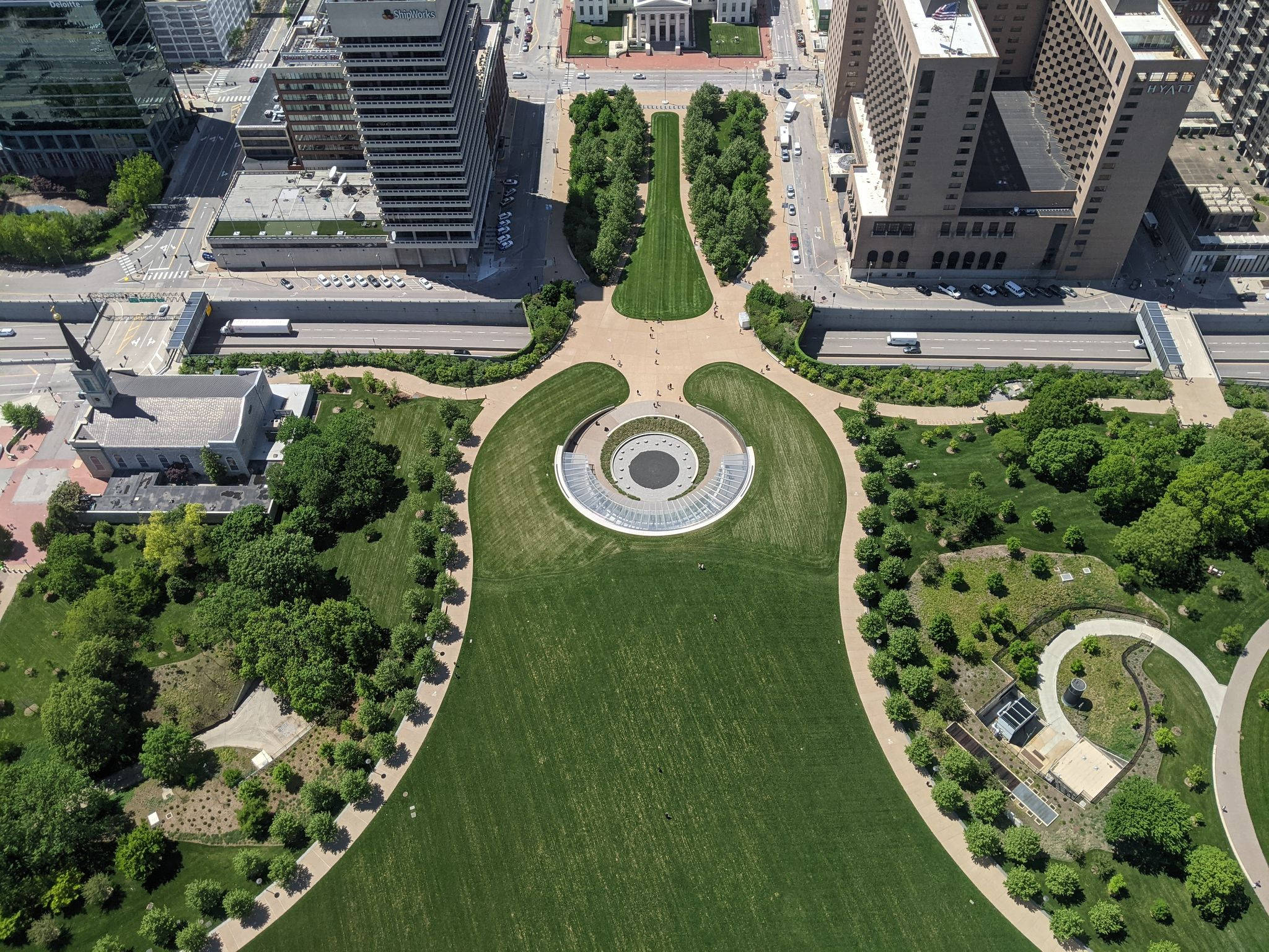 建築 桌布 壁紙 — 現代城市公園的鳥瞰圖，擁有茂密的綠色草坪、蜿蜒小徑和一個被高樓大廈環繞的圓形廣場。