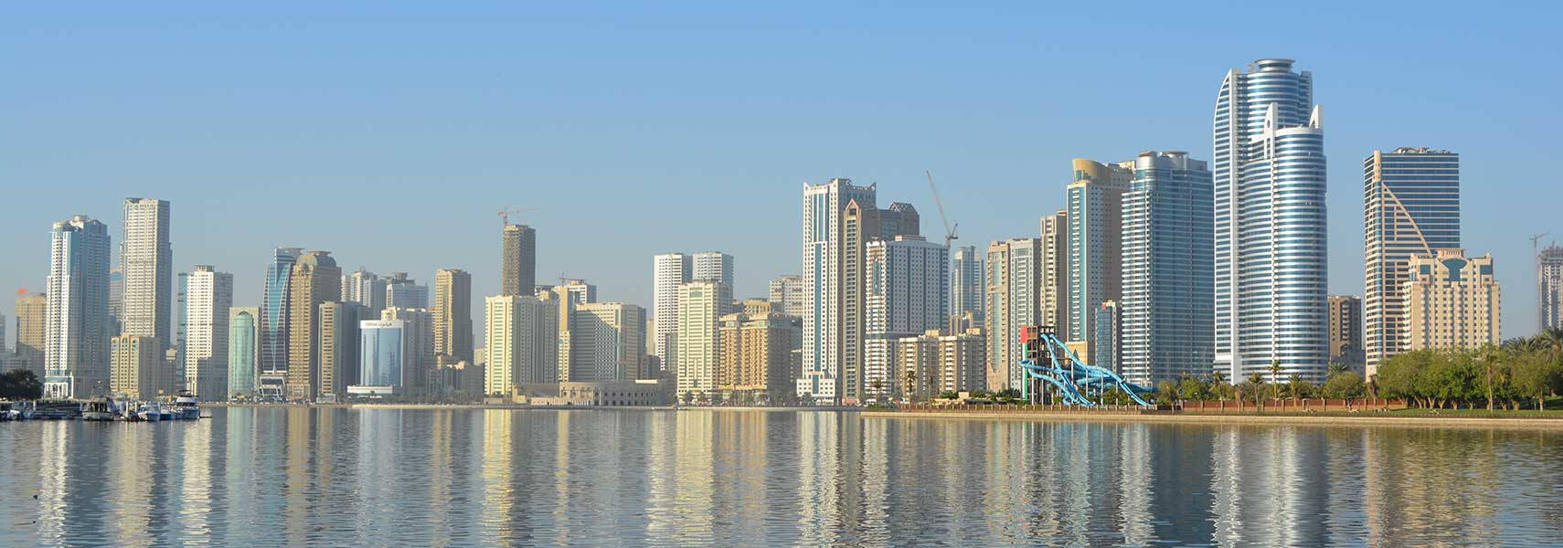 Buildings 桌布 壁紙 — 現代城市天際線，玻璃摩天大樓倒映在平靜的水面上，天空清澈湛藍。