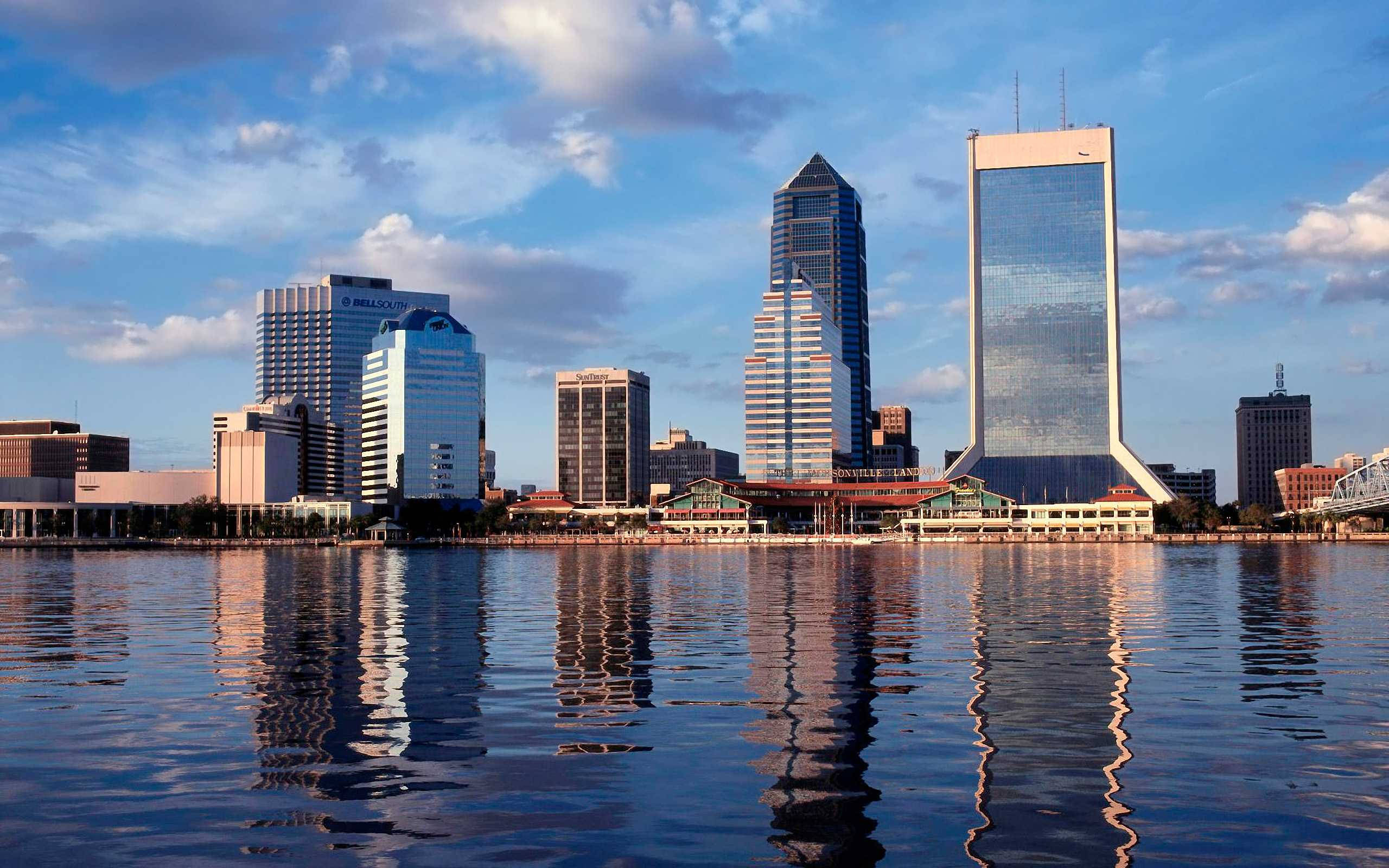 Jacksonville 桌布 壁紙 — 現代城市天際線，玻璃摩天大樓倒映在平靜的水面上，天空多雲，藍天白雲。
