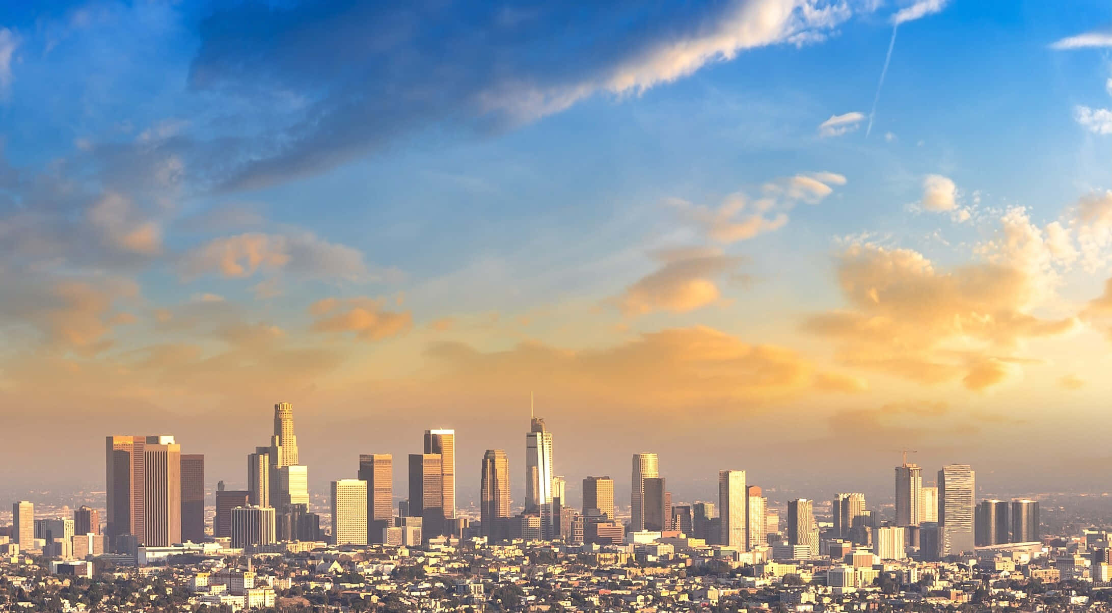 城市 桌布 壁紙 — 現代城市天際線的 panoramic 景觀，夕陽西下，金色雲彩和高聳的摩天大樓。