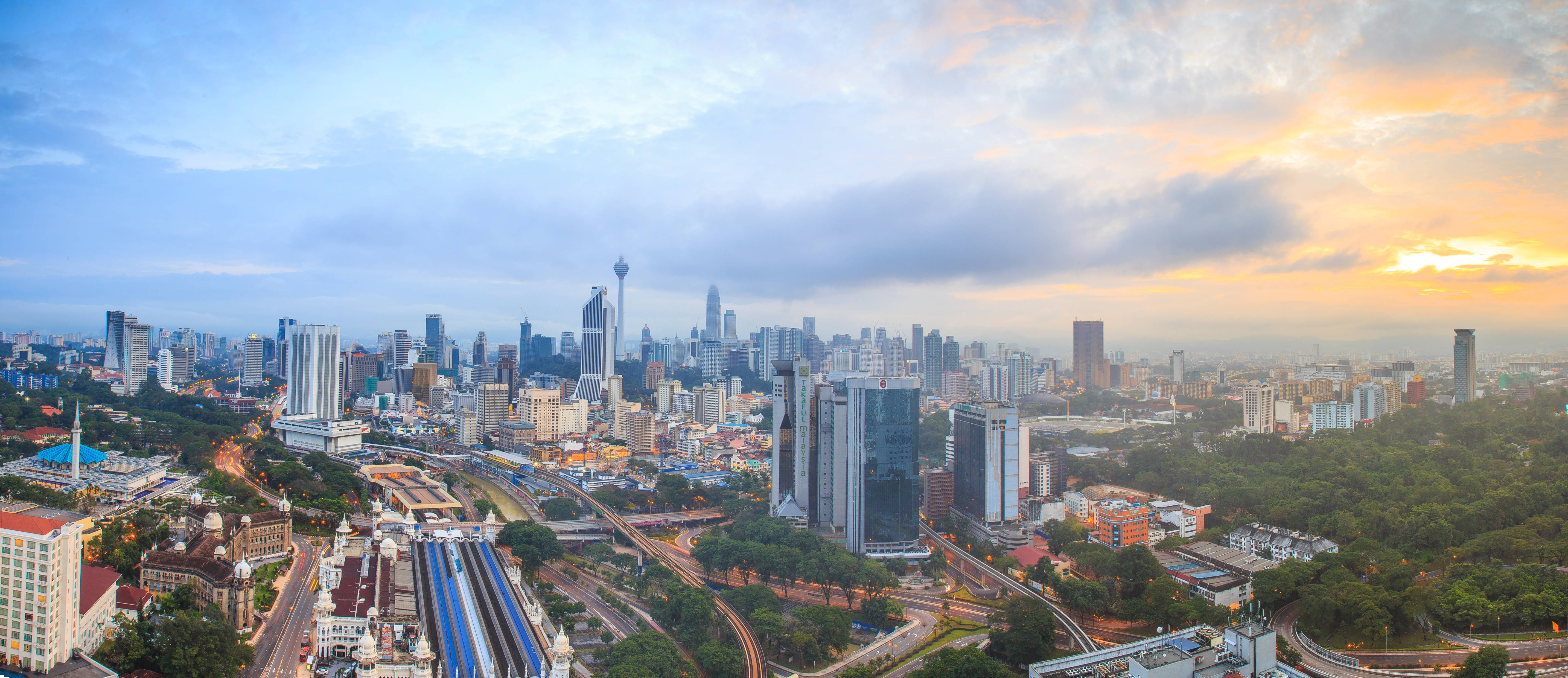馬來西亞 桌布 壁紙 — 現代城市天際線的 panoramic 景觀，夕陽西下，金色雲彩和高聳的摩天大樓。
