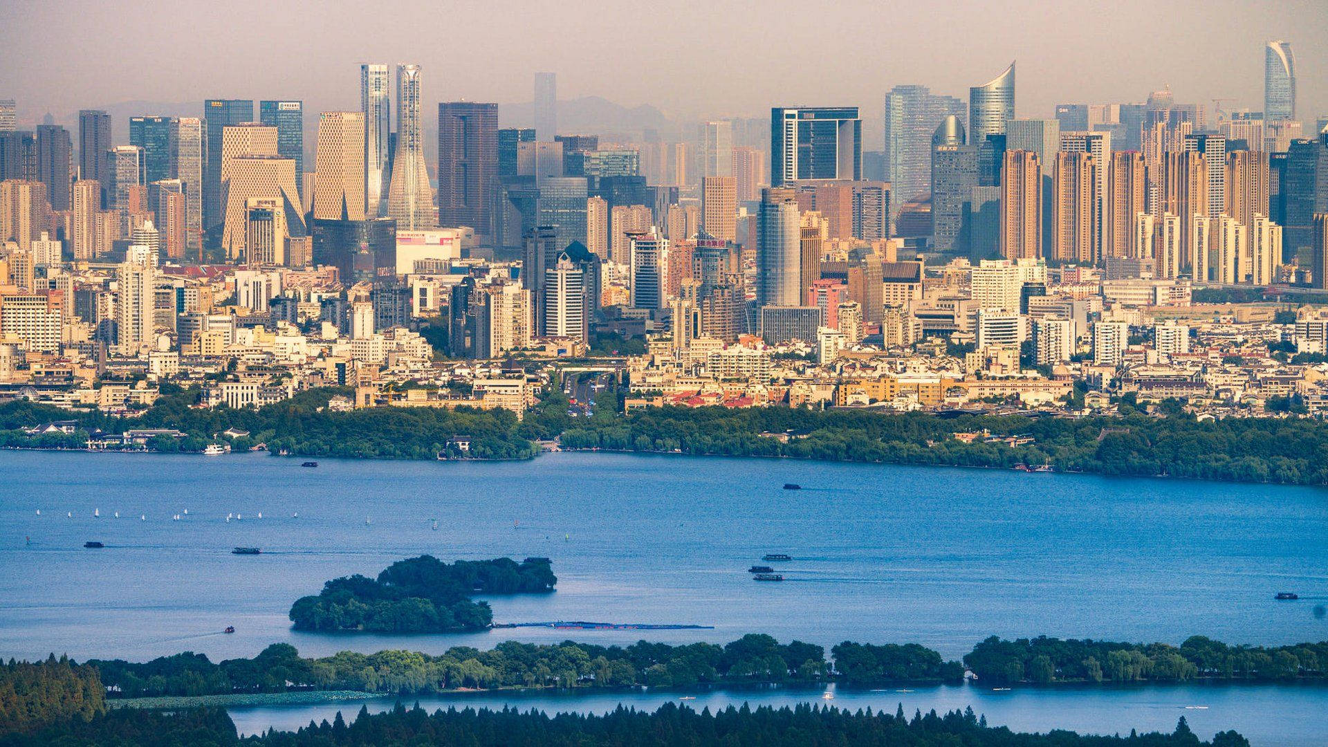 Hangzhou 桌布 壁紙 — 現代城市天際線的全景視圖，在廣闊的藍色湖泊後面升起，湖泊上點綴著小船和綠色島嶼。