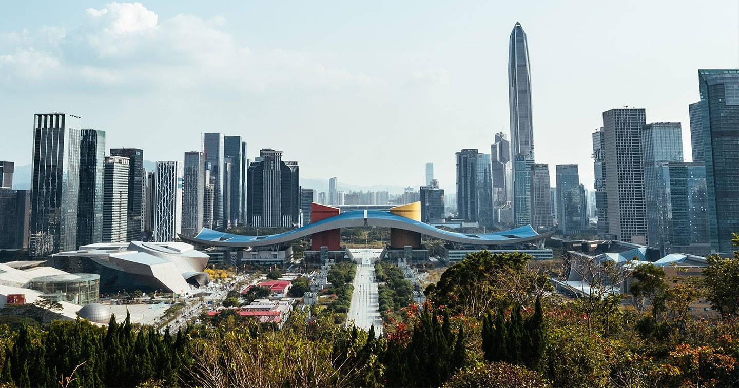 Shenzhen 桌布 壁紙 — 現代城市天際線的全景視圖，玻璃摩天大樓和色彩繽紛的未來主義橋樑在部分多雲的天空下。