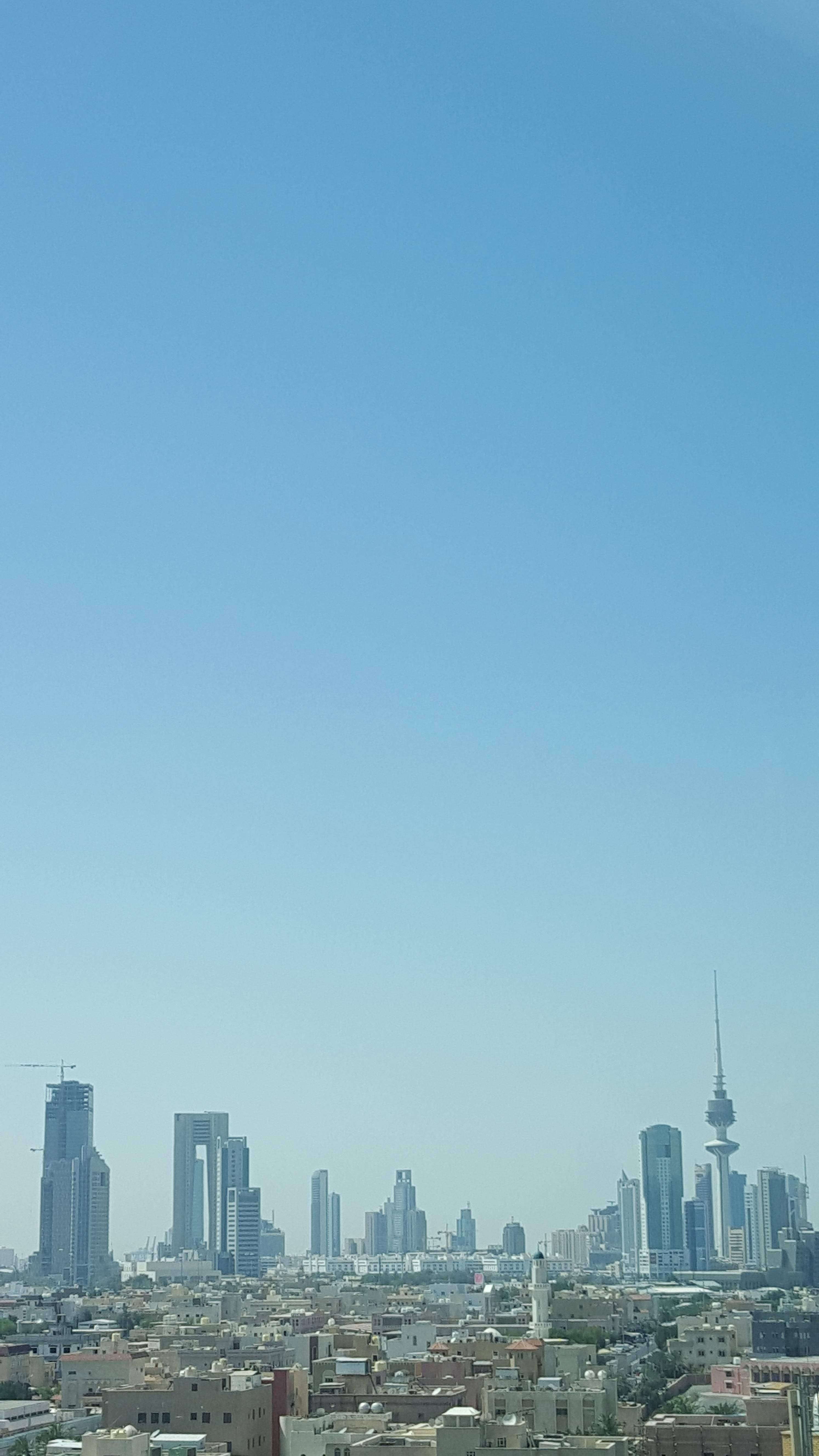 科威特 桌布 壁紙 — 現代城市天際線的全景視圖，高聳的摩天大樓和一座突出的塔樓，在廣闊清澈的藍天下。