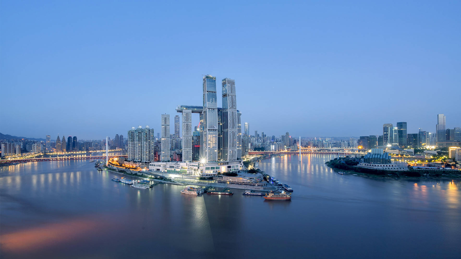 Chongqing 桌布 壁紙 — 現代城市天際線的黃昏全景，倒映在寬闊的河流中，閃爍的摩天大樓和船隻。