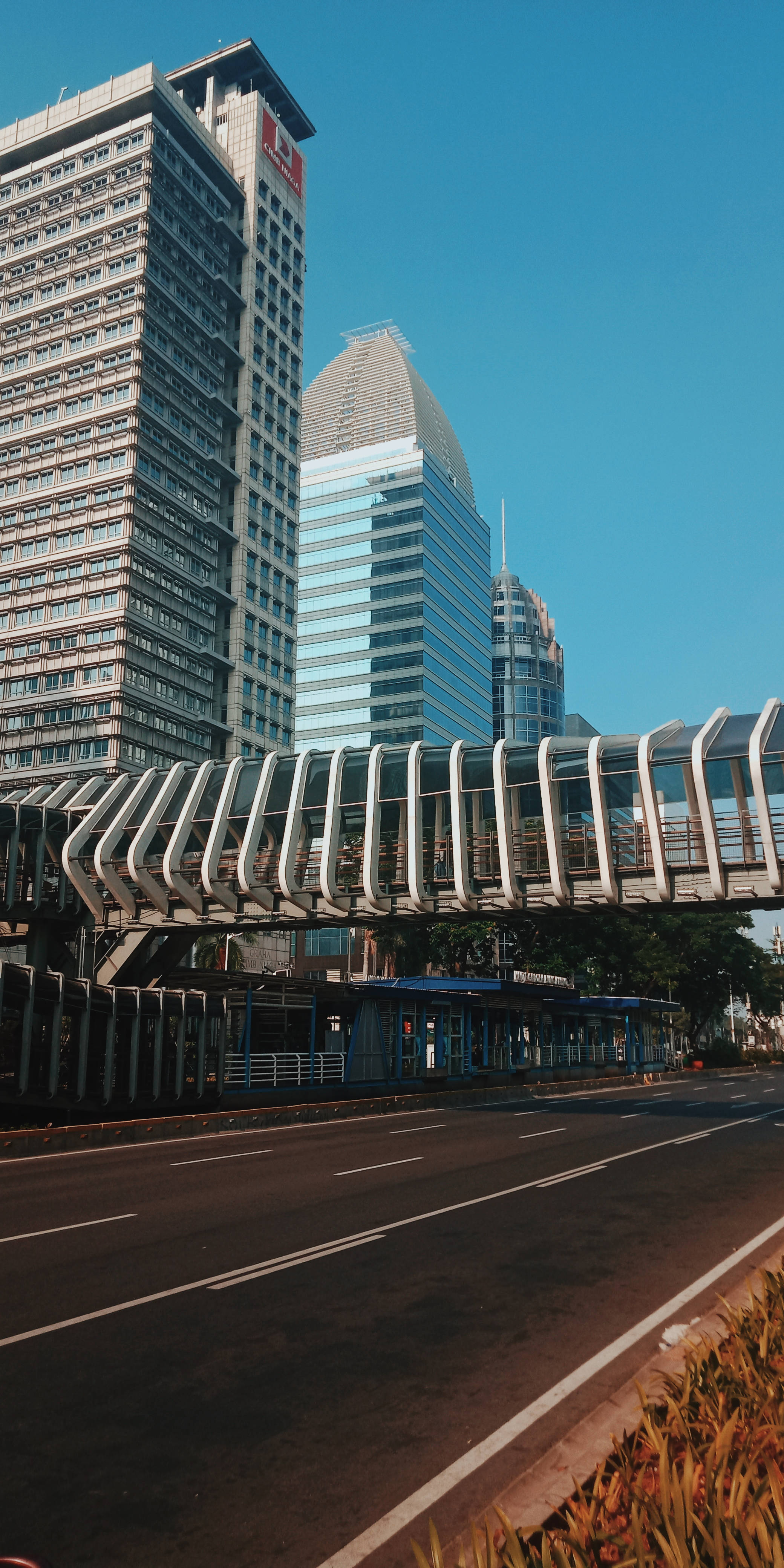 Morning 桌布 壁紙 — 現代城市景觀，玻璃摩天大樓和彎曲的人行天橋在晴朗的藍天下。