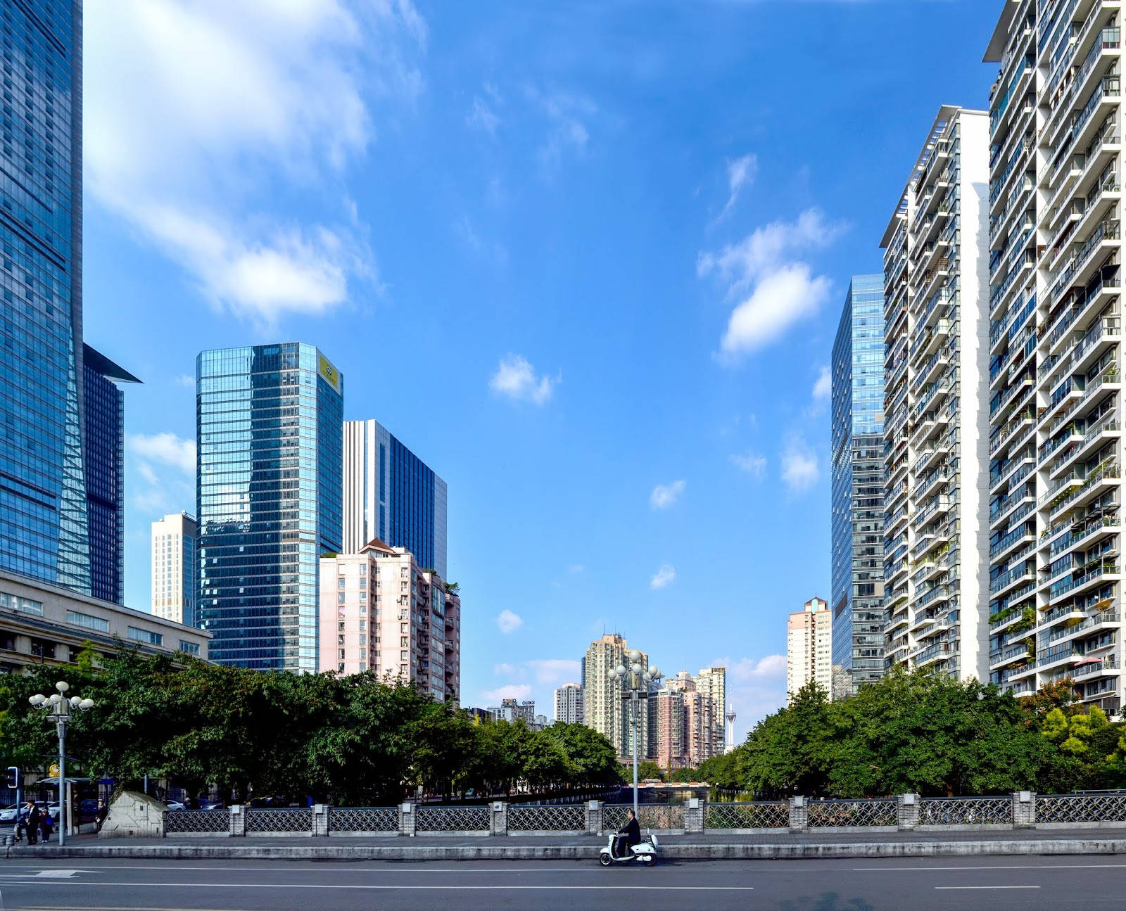 Chengdu 桌布 壁紙 — 現代城市景觀，高聳的玻璃摩天大樓和住宅塔樓，在明亮的藍天和零星白雲下。