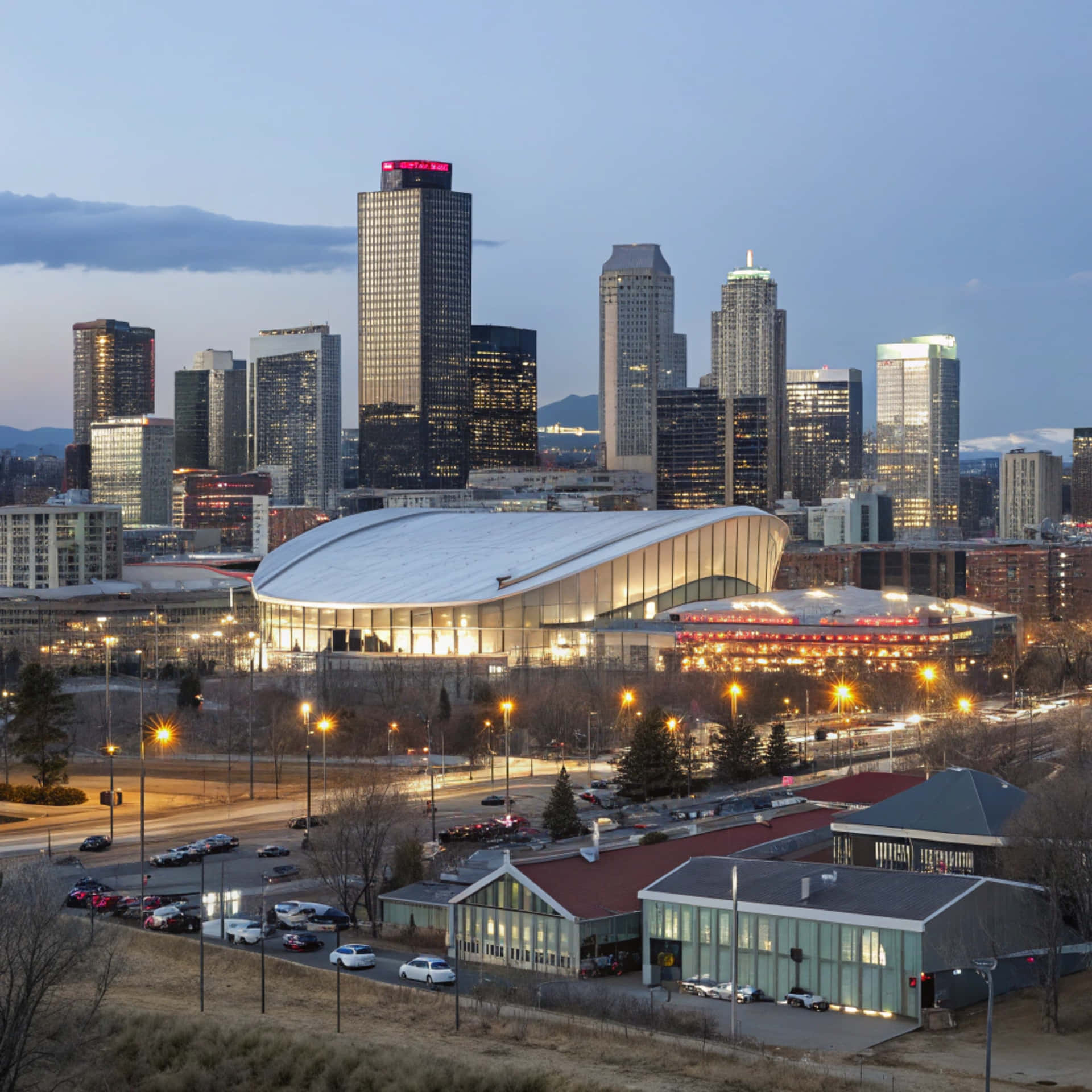 Denver Skyline 壁紙 — 現代城市景觀，黃昏時分，摩天大樓燈火通明，彎曲的體育館在暮色中溫暖地發光。