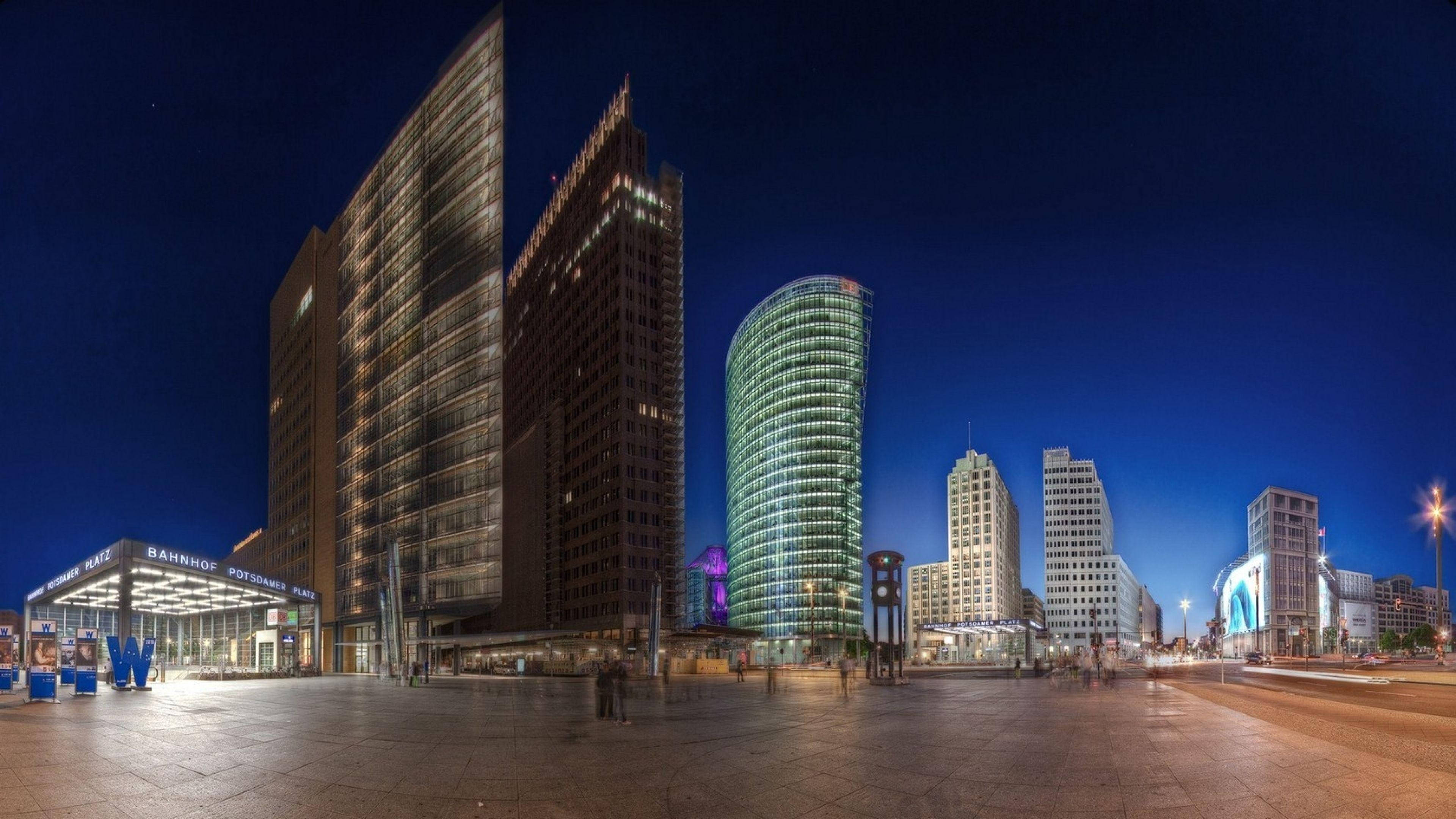 Berlin 桌布 壁紙 — 現代城市景觀的 panoramic 夜景，在深藍色天空下，有燈火通明的摩天大樓和寬闊的廣場。