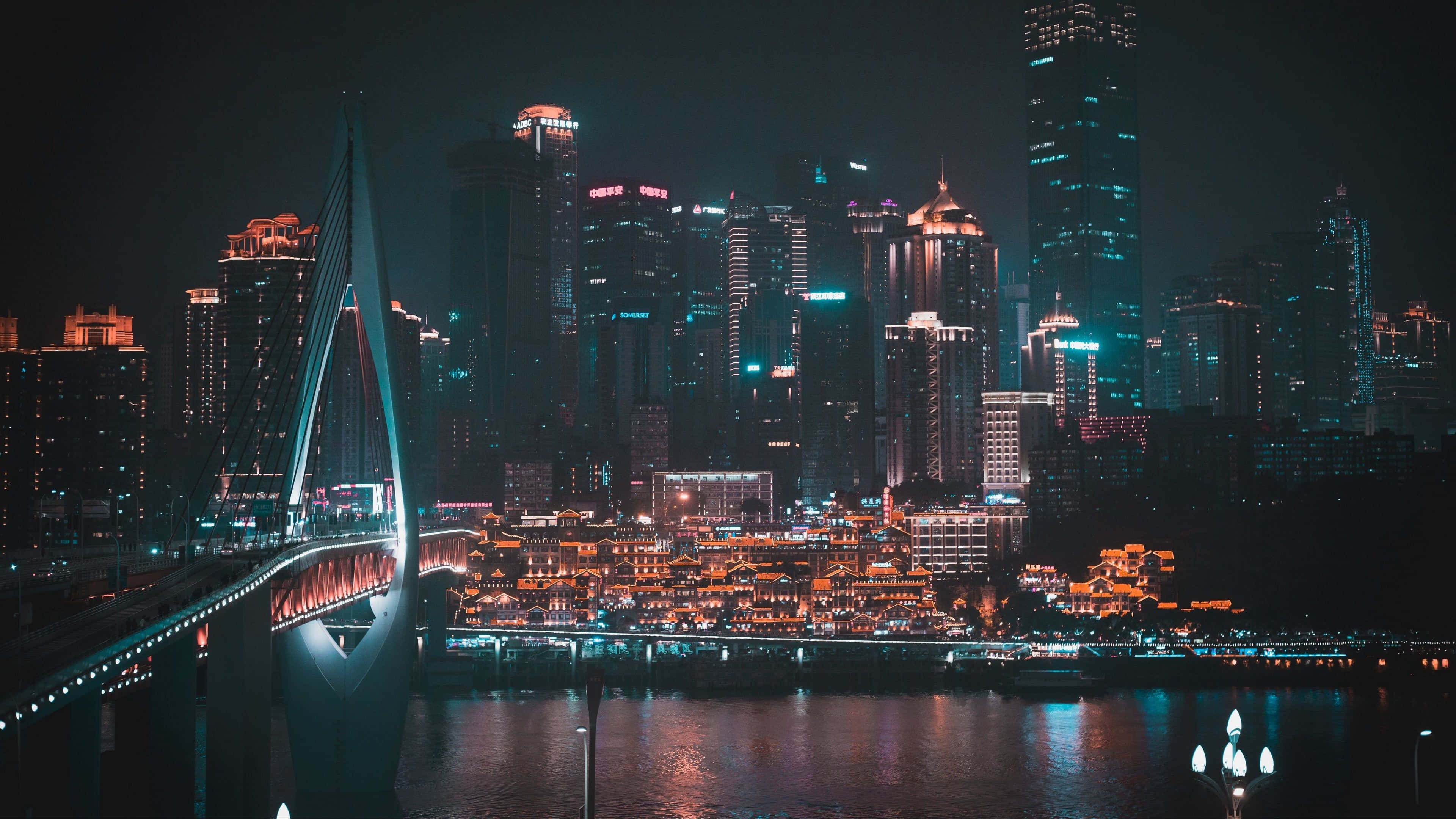 City Night 桌布 壁紙 — 現代城市景觀的壯麗夜景，一座發光的橋樑橫跨河流，反射著高聳摩天大樓的霓虹燈光。