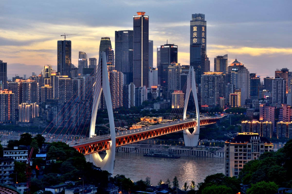 Chongqing 桌布 壁紙 — 現代城市景觀的壯麗日落景色，一座發光的斜張橋橫跨河流，周圍是高聳的摩天大樓。