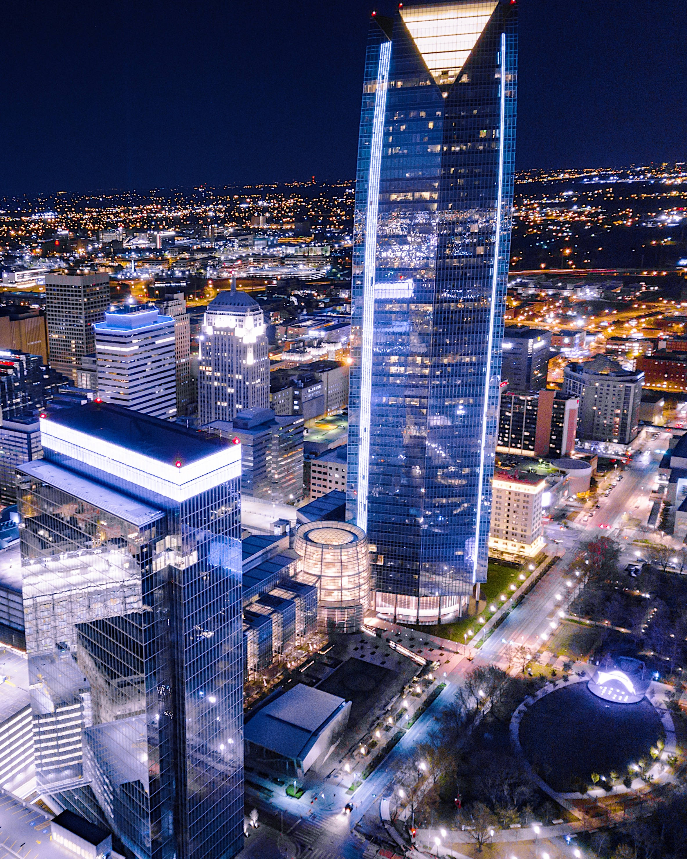Oklahoma 桌布 壁紙 — 現代城市景觀的空中夜景，以一座高聳的玻璃摩天大樓為主，散發著藍色光芒。