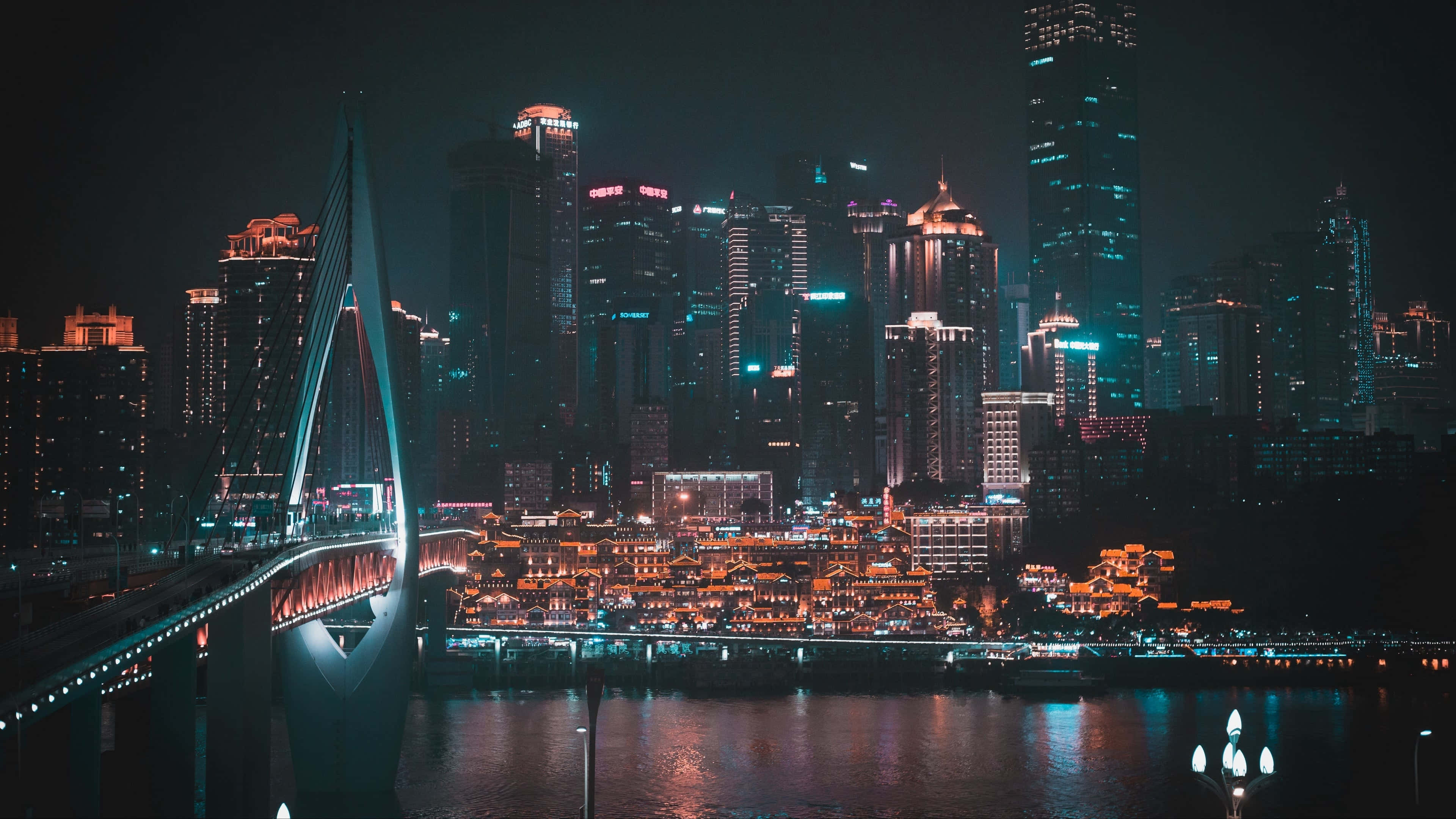 城市 桌布 壁紙 — 現代城市景觀的迷人夜景，一座發光的橋樑橫跨河流，反射著摩天大樓和傳統建築的霓虹燈光。