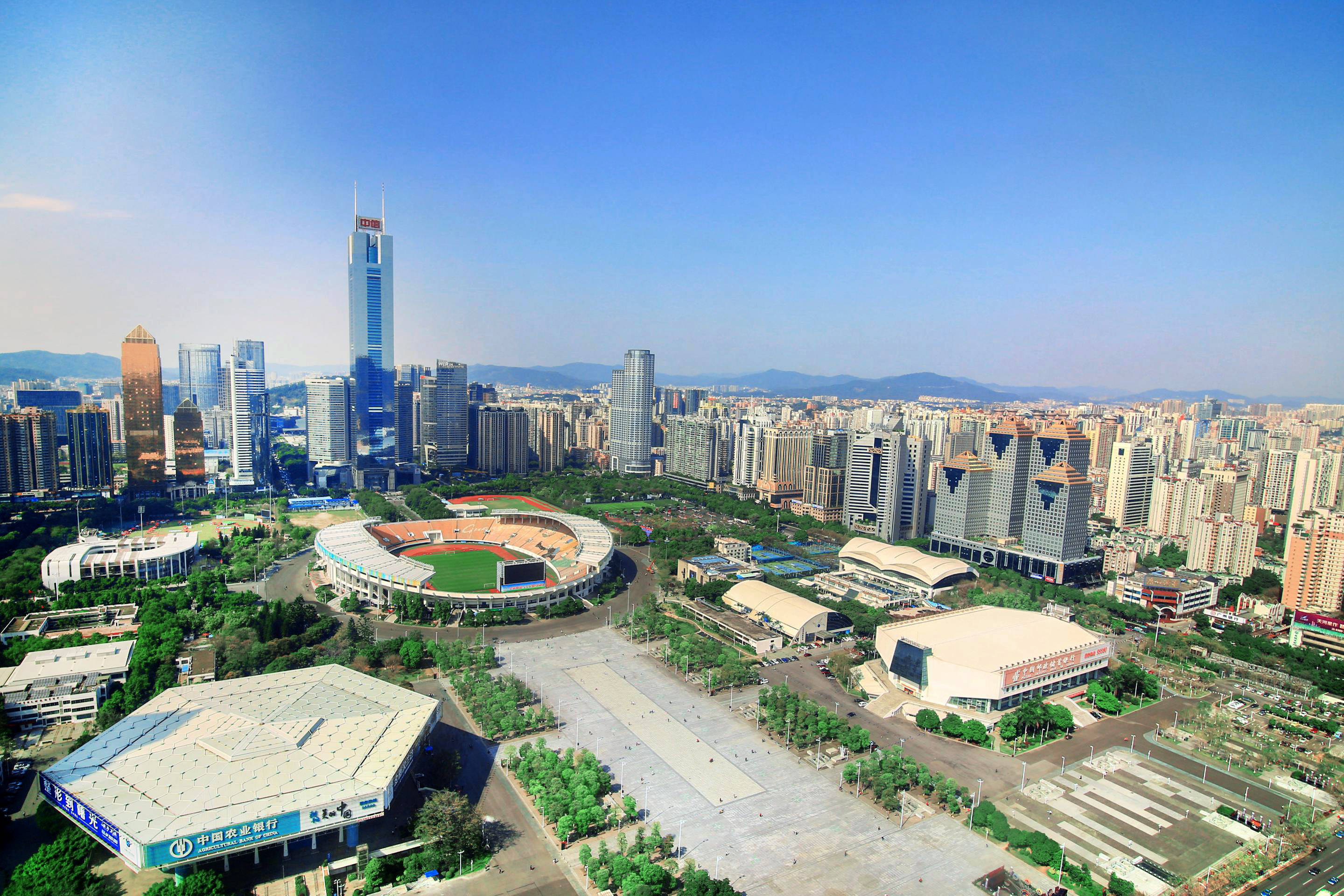 Guangzhou 桌布 壁紙 — 現代城市景觀的鳥瞰圖，包括摩天大樓、一個大型體育館和綠地，在晴朗的藍天下。