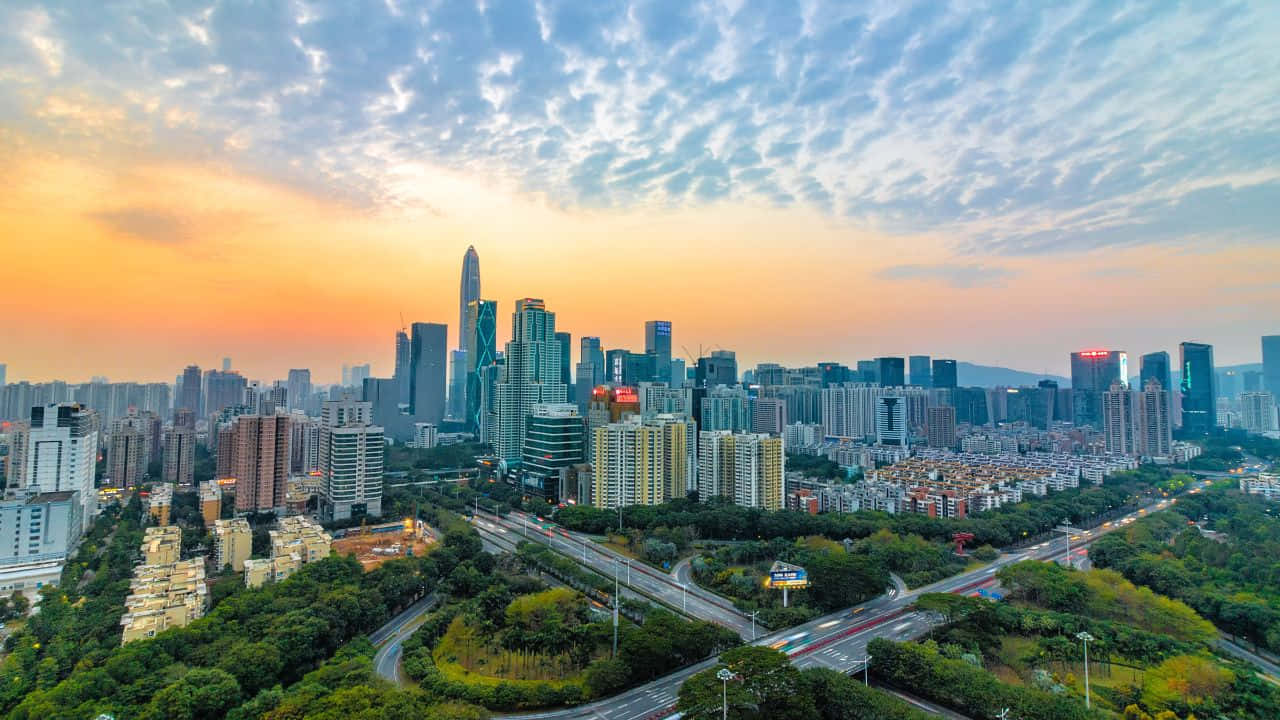 1280x720 桌布 壁紙 — 現代城市景觀的鳥瞰圖，夕陽西下，高聳的摩天大樓和鬱鬱蔥蔥的公園在充滿活力的橙色和藍色天空下。
