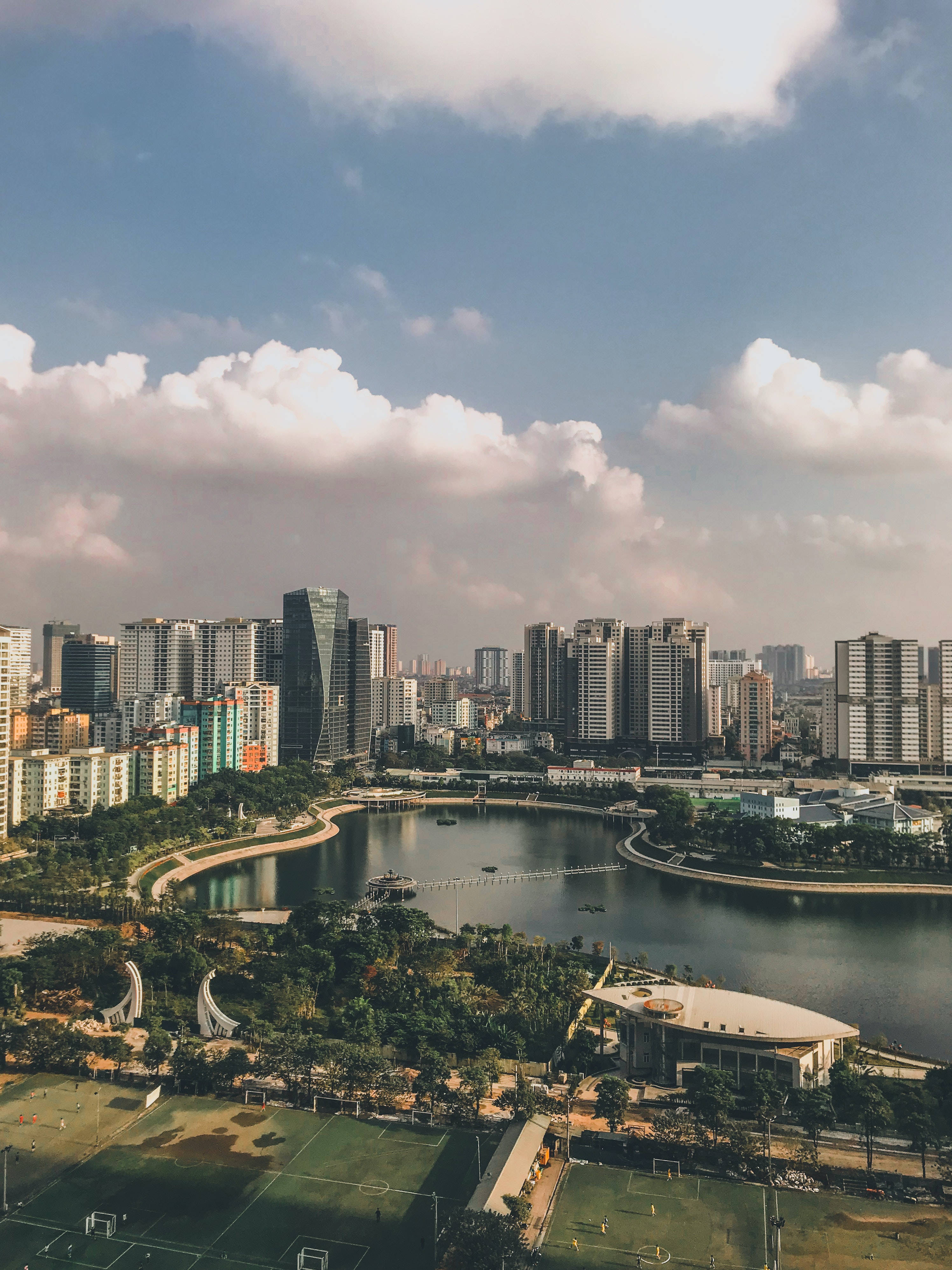 iPhone 桌布 壁紙 — 現代城市景觀的鳥瞰圖，有一條蜿蜒的河流，周圍是綠色公園和運動場，天空部分多雲。