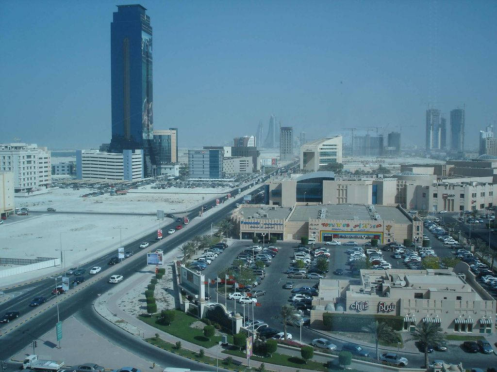 Bahrain 桌布 壁紙 — 現代城市景觀的鳥瞰圖，高樓大廈、繁忙道路和停車場在朦朧的藍天下。