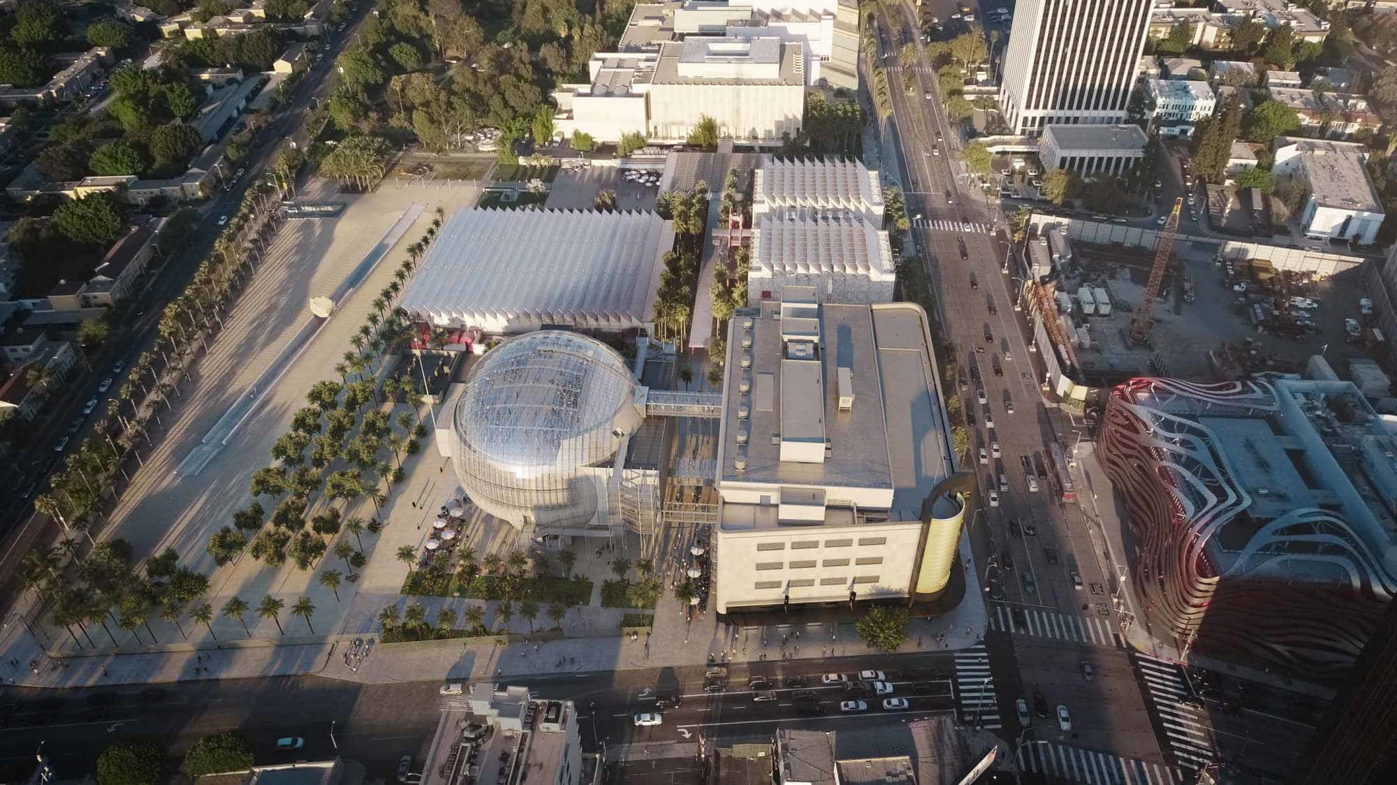 Top View 桌布 壁紙 — 現代城市綜合體的鳥瞰圖，有一座玻璃穹頂建築，周圍環繞著棕櫚樹和繁忙的街道。
