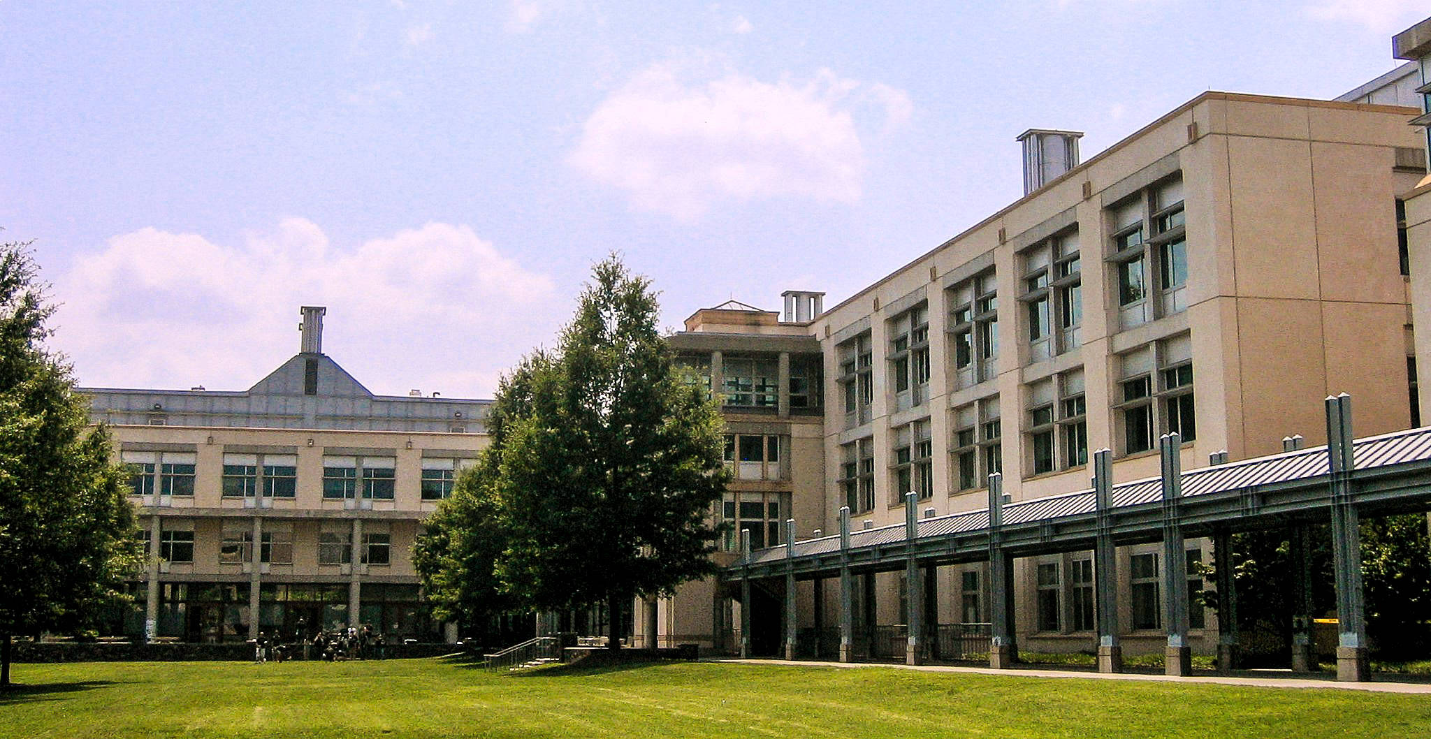設計 桌布 壁紙 — 現代大學建築，玻璃窗和米色石牆，在明亮的藍天和白雲下，周圍是茂密的綠色草坪和高大的樹木。