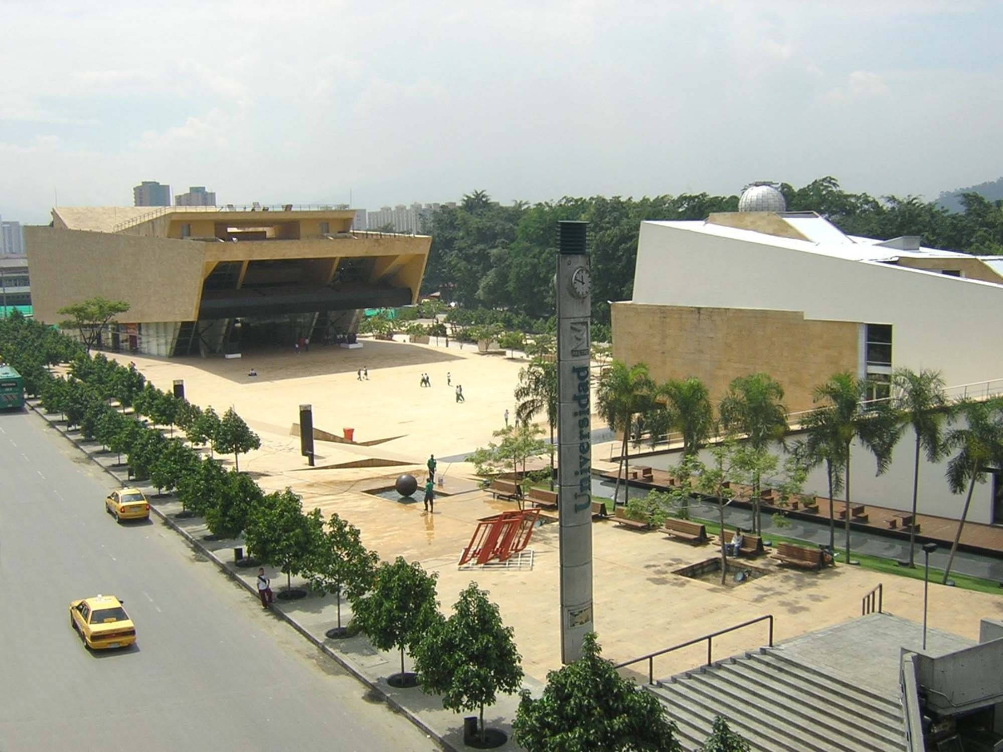 Medellin 桌布 壁紙 — 現代大學校園，擁有醒目的棱角建築、棕櫚樹和黃色計程車，在晴朗的日子。