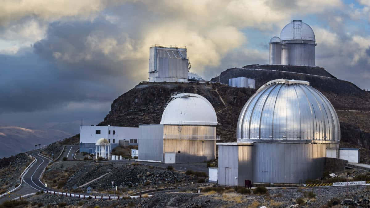 Observatory 桌布 壁紙 — 現代天文台圓頂在戲劇性的暮色雲層下，於崎嶇的山脊上閃耀。