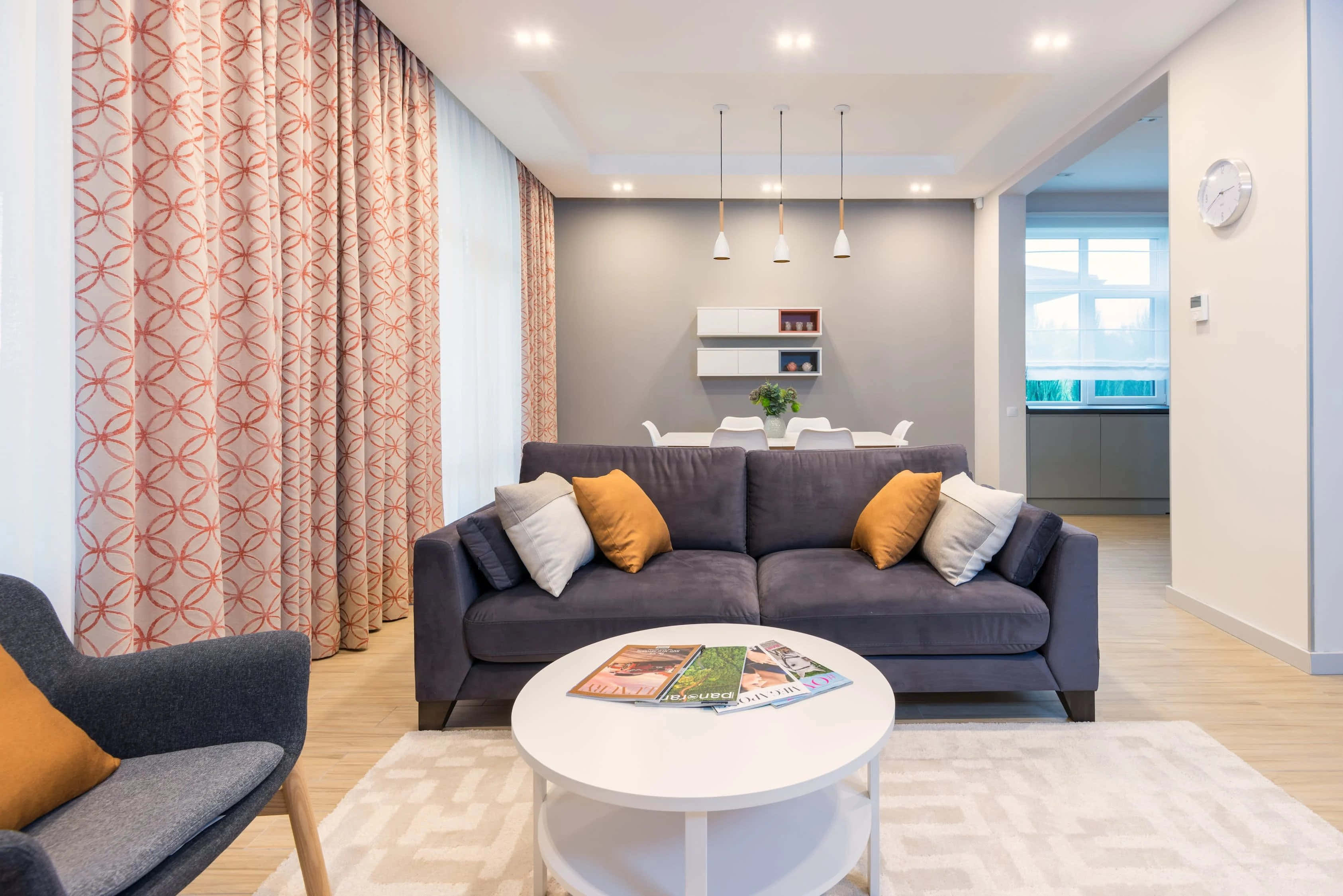 Apartment 桌布 壁紙 — 現代客廳，配有灰色沙發、橙色枕頭、圖案窗簾和白色茶几，上方有明亮的吊燈。