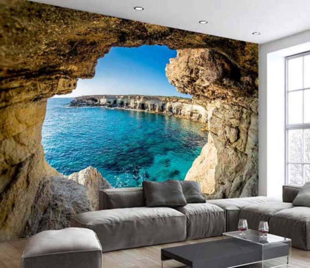 Interior Design 桌布 壁紙 — 現代客廳設有巨大的洞穴牆壁壁畫，在清澈的藍天下展現出充滿活力的碧綠海洋和岩石懸崖。