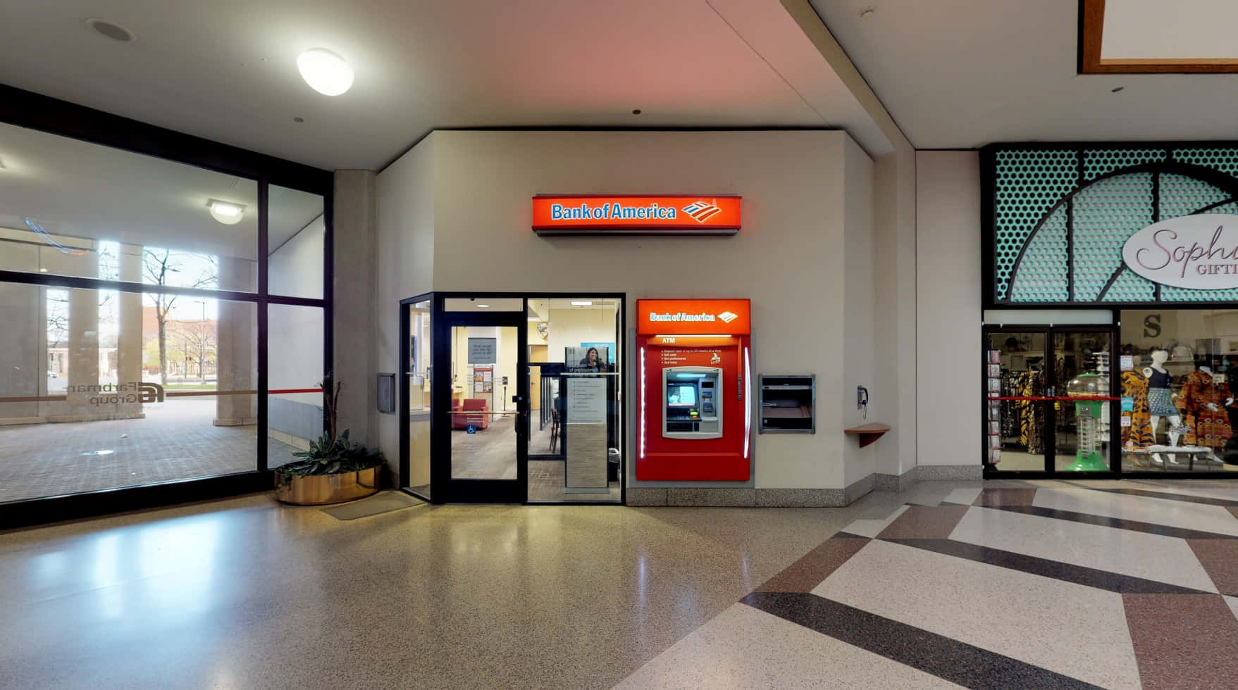 Bank Of America 桌布 壁紙 — 現代室內購物中心走廊，設有亮紅色 Bank of America 自動櫃員機及入口，旁邊是有人體模型的禮品店。