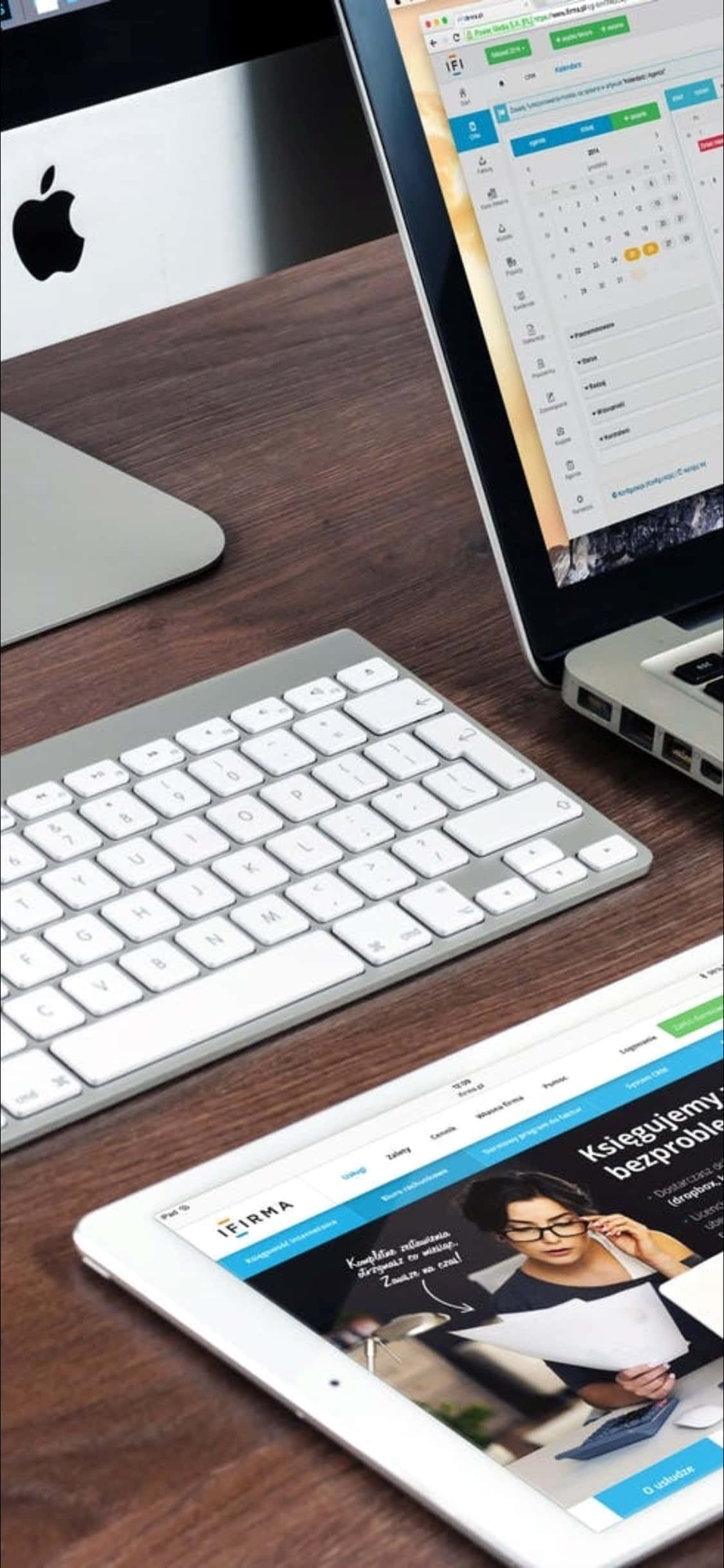Desk 桌布 壁紙 — 現代工作空間，深色木桌上擺放銀色筆記型電腦、平板電腦和鍵盤，顯示數位內容。