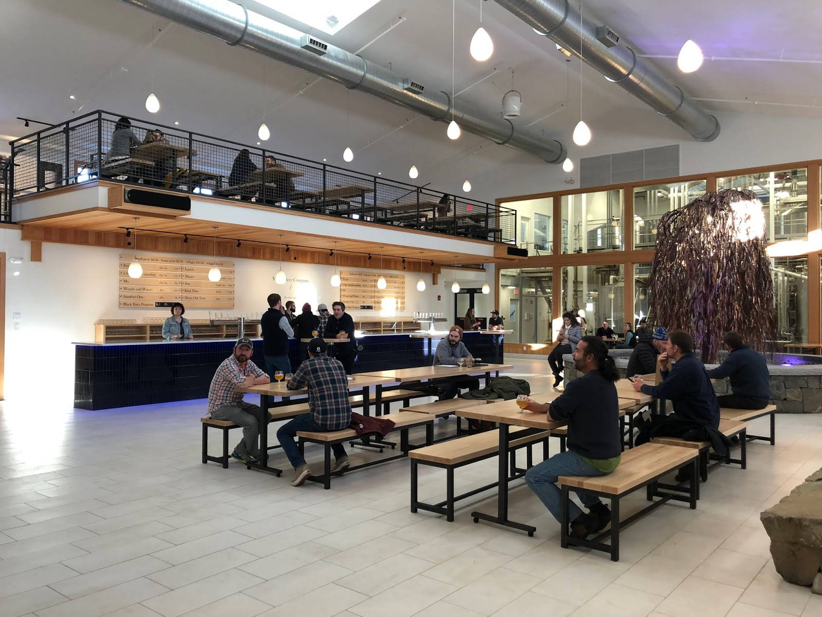 建築 桌布 壁紙 — 現代工業風食堂，人們在木桌用餐，上方有裸露管道和吊燈。