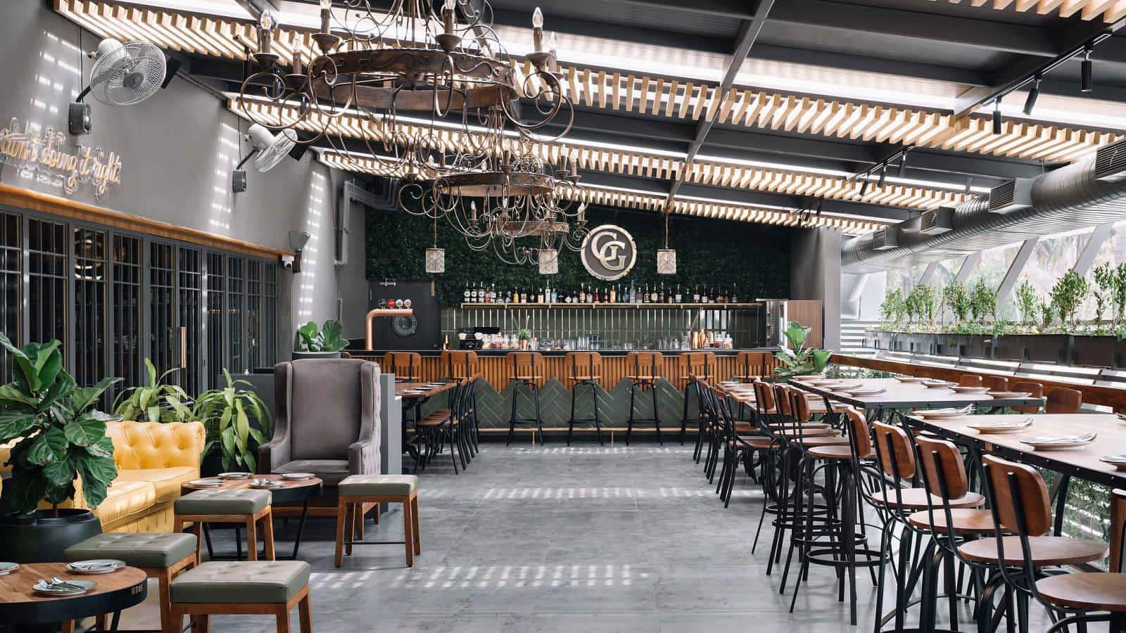 Interior Design 桌布 壁紙 — 現代工業風餐廳內部，設有裸露橫樑、吊燈，以及沿吧檯和座位區排列的綠色植物。
