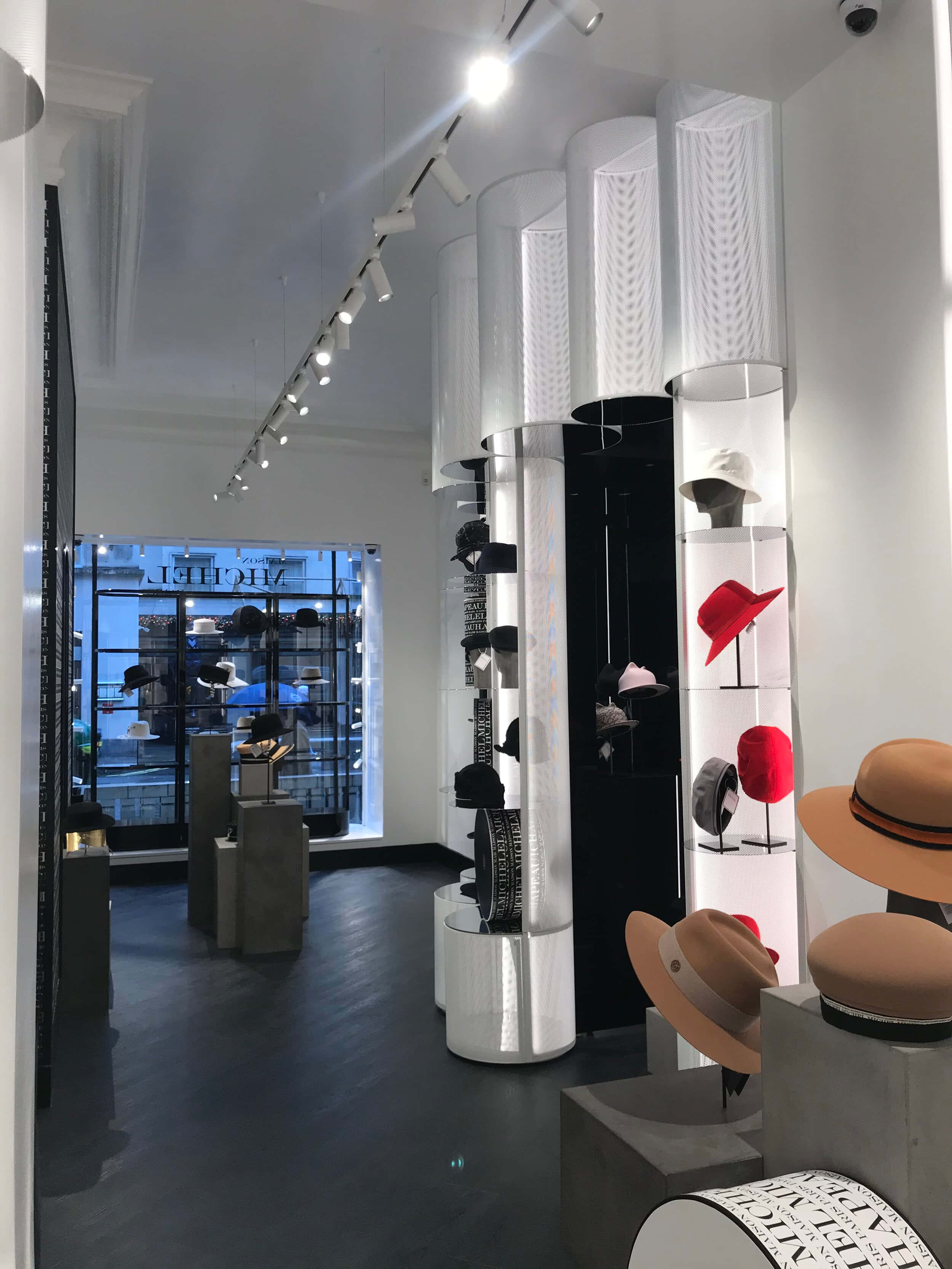 Clothes 桌布 壁紙 — 現代帽子精品店，採用時尚白色柱子，在明亮的軌道燈光下展示色彩繽紛的帽子。