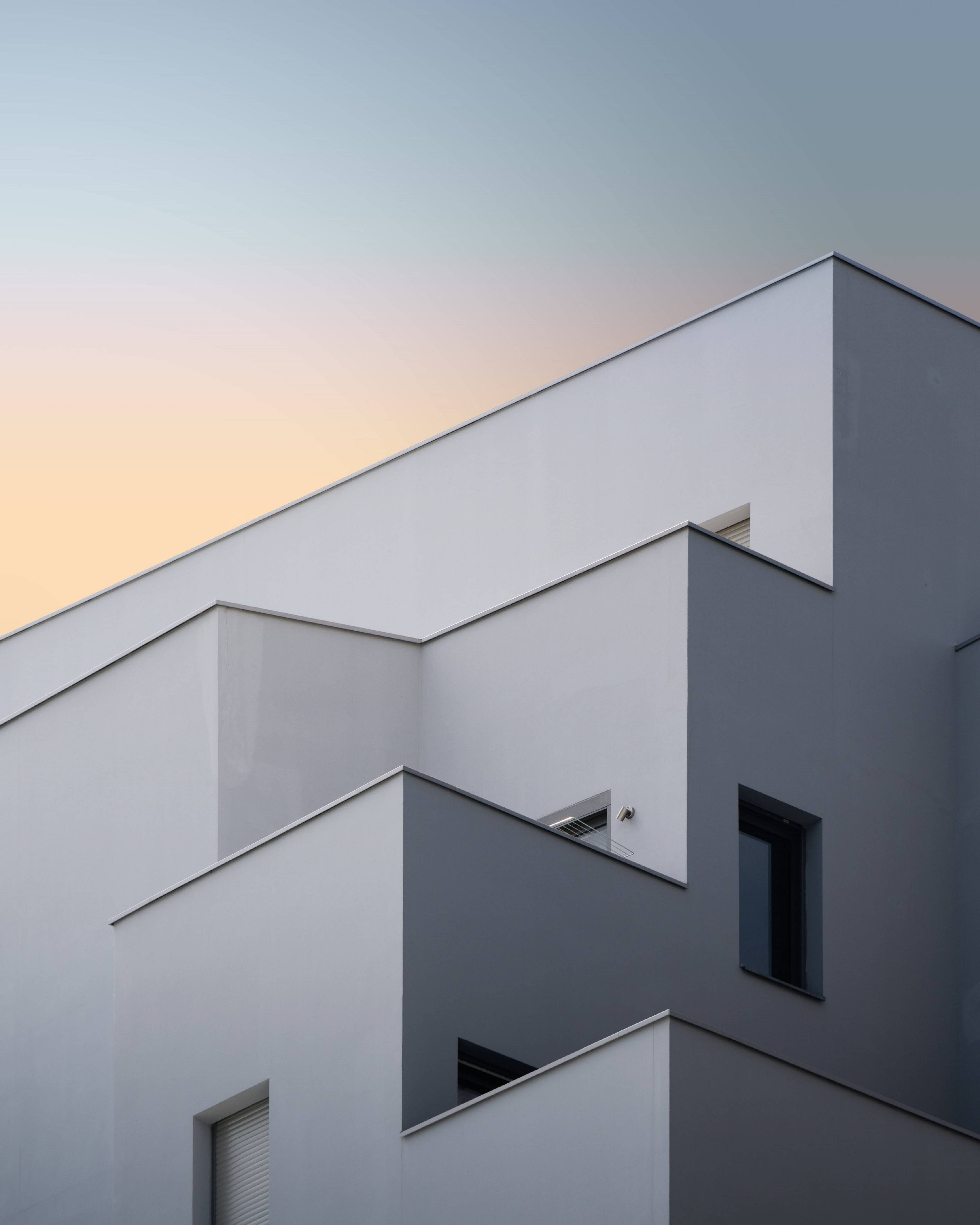 Architecture 桌布 壁紙 — 現代幾何建築外牆，以純淨的白色和灰色平面襯托柔和的日落天空。
