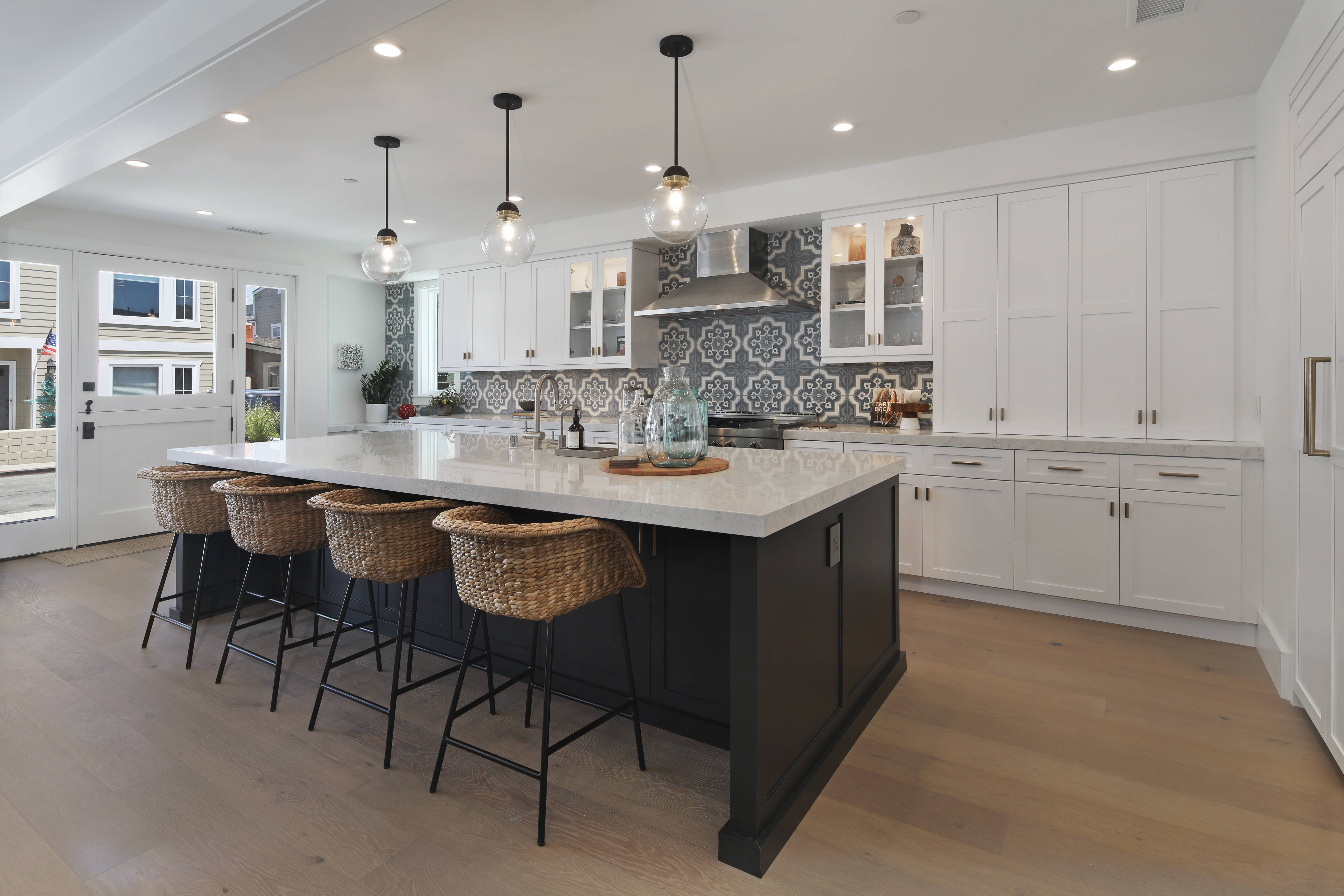 Kitchen Design 桌布 壁紙 — 現代廚房，白色櫥櫃，黑色中島，藤編吧檯椅，圖案瓷磚防濺牆，下方明亮吊燈。