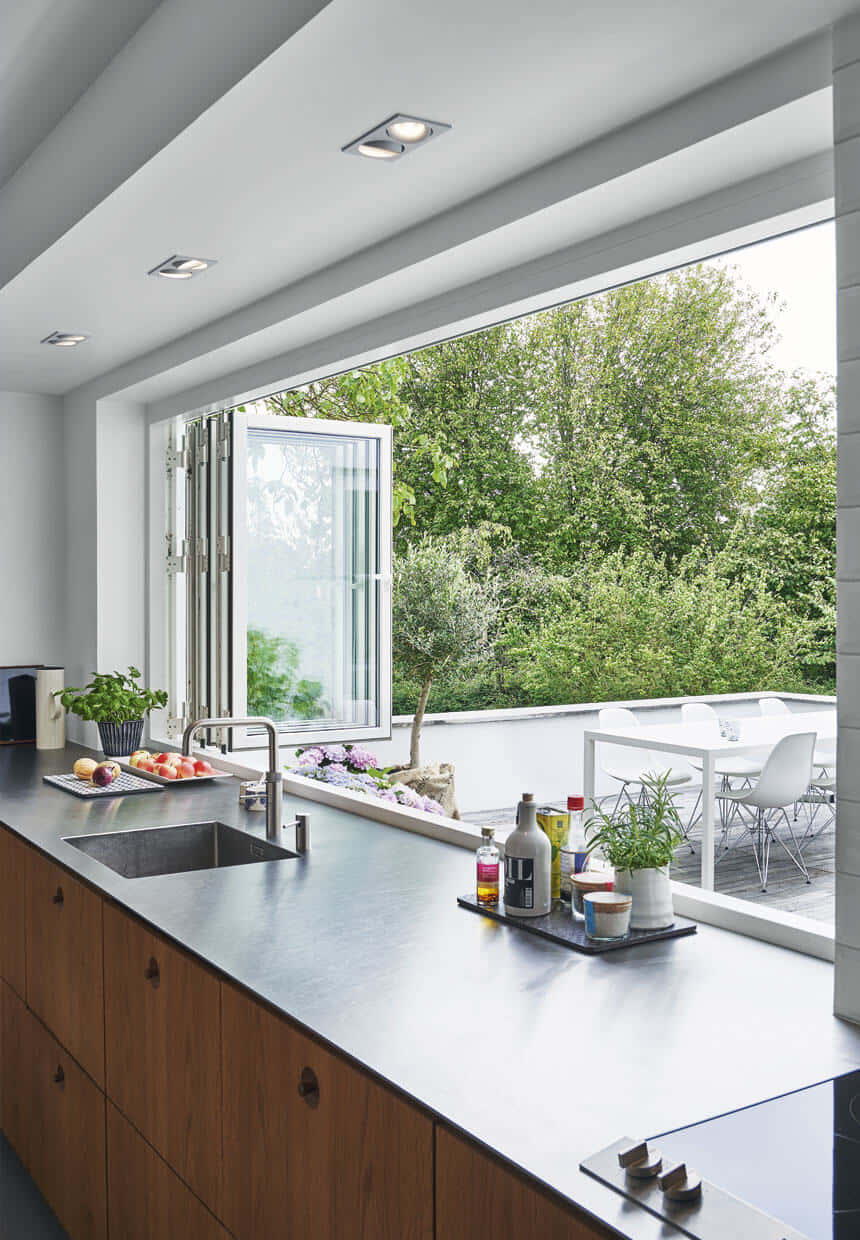 Kitchen Design 桌布 壁紙 — 現代廚房，配有木製櫥櫃和不鏽鋼檯面，透過大玻璃窗俯瞰鬱鬱蔥蔥的綠色花園。