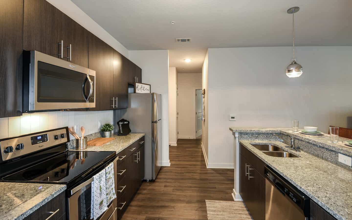 1440p Kitchen 桌布 壁紙 — 現代廚房，配有深色木櫃、不鏽鋼電器和花崗岩檯面，在溫暖的吊燈照明下。