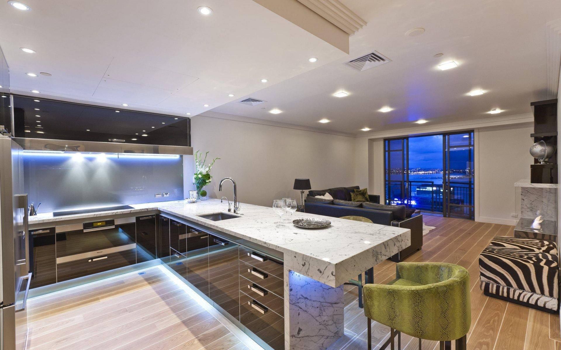 Kitchen Design 桌布 壁紙 — 現代廚房和起居區，配有大理石島檯，在LED燈光下閃耀，俯瞰城市夜景。